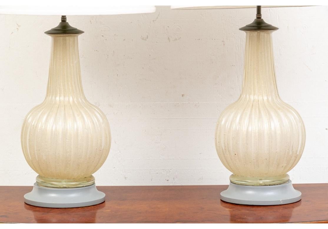 Tischlampen mit zwei Leuchten, gerippte Melonenformen mit hohen Hälsen aus elegantem, klassischem Murano-Goldglas. Montiert auf grau lackierten Holzsockeln. Mit weißen Trommelschirmen aus Stoff. 
Maße: Höhe. 31 1/4