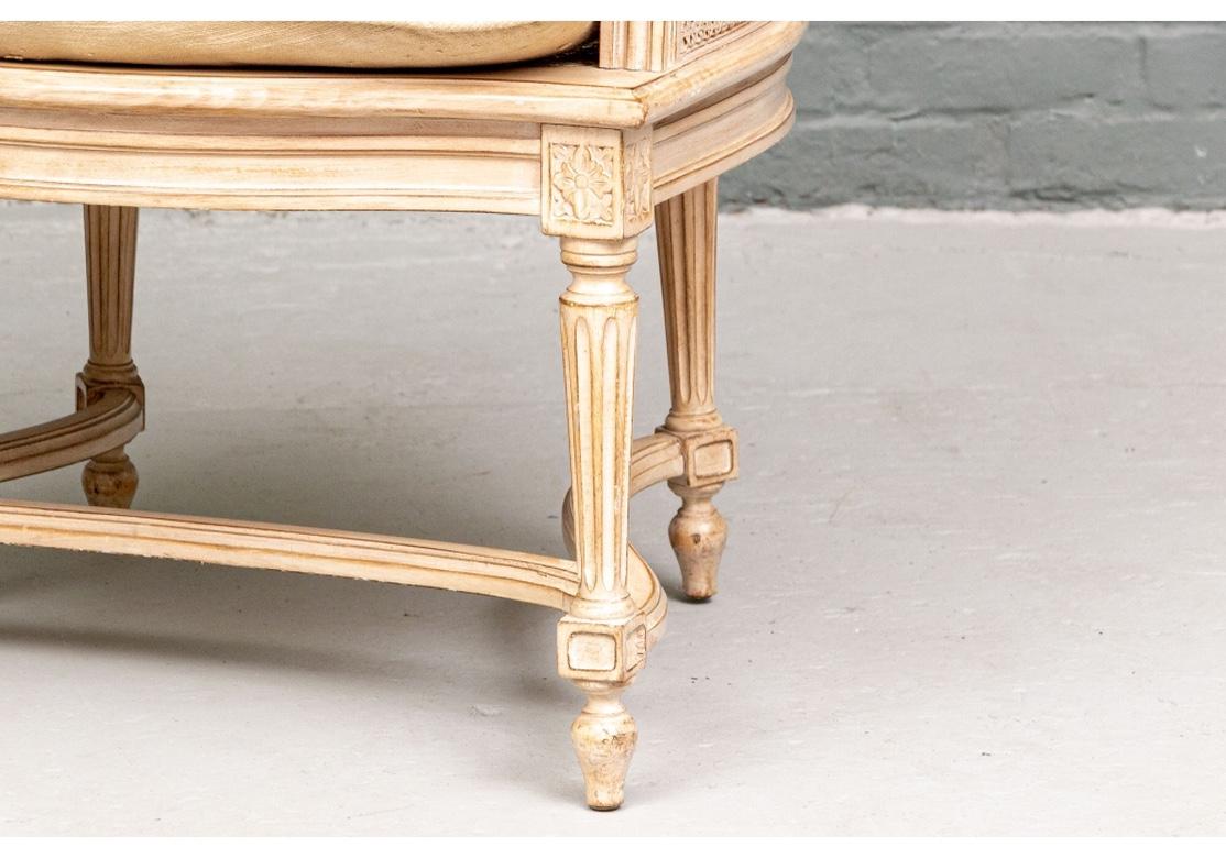 With wide square backs, the carved frames with bow crests and ribbed scrolled arms. The bleached frame with serpentine skirt rails raised on fluted tapering legs with shaped three part stretchers. Caned backs, arms and seats. With pale raw silk type