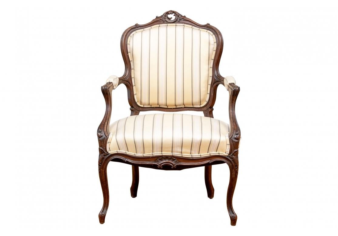The elegant Louis XV style armchair with a carved and scrolled crest rail with open cartouche in the center. The sloping arms with scrolls and the ends with carved acanthus leaves. Raised on cabriole front legs with carved acanthus leaves on the