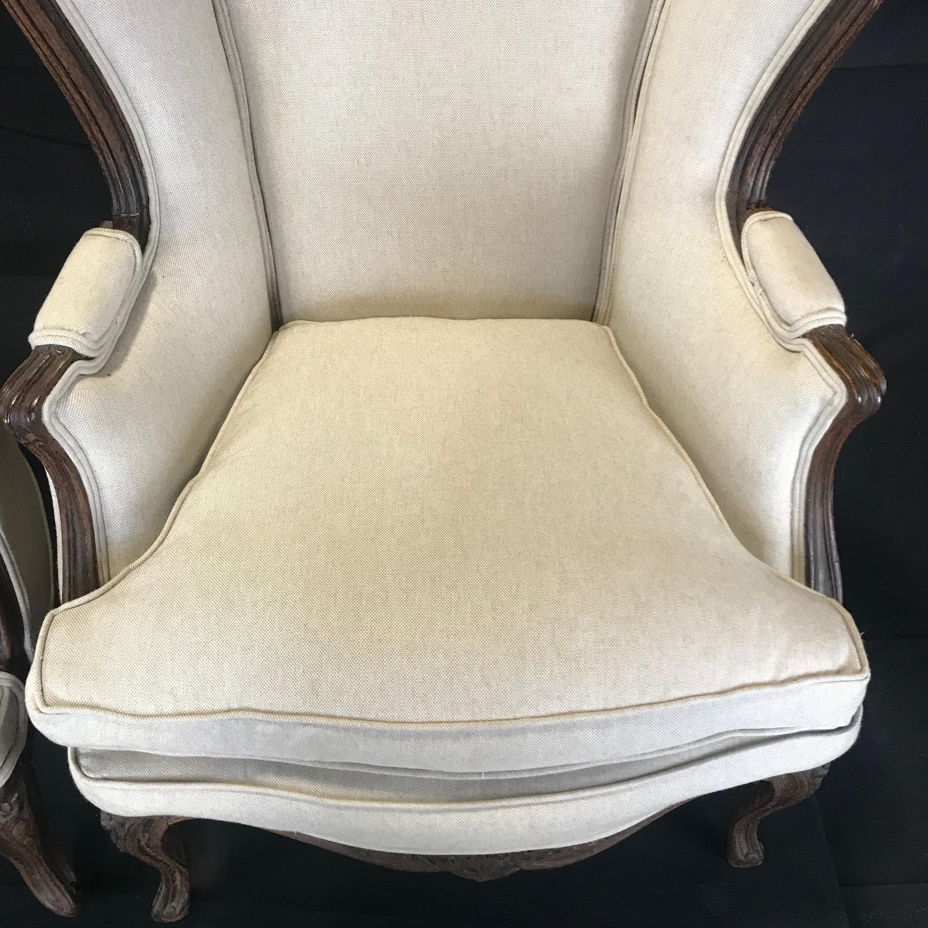 Finely carved 19th century French Louis XV wingback armchairs newly upholstered in linen with down cushions, French, circa 1870. A pair of decorative and well carved solid walnut wing back armchairs, having a shaped back with winged show wood sides