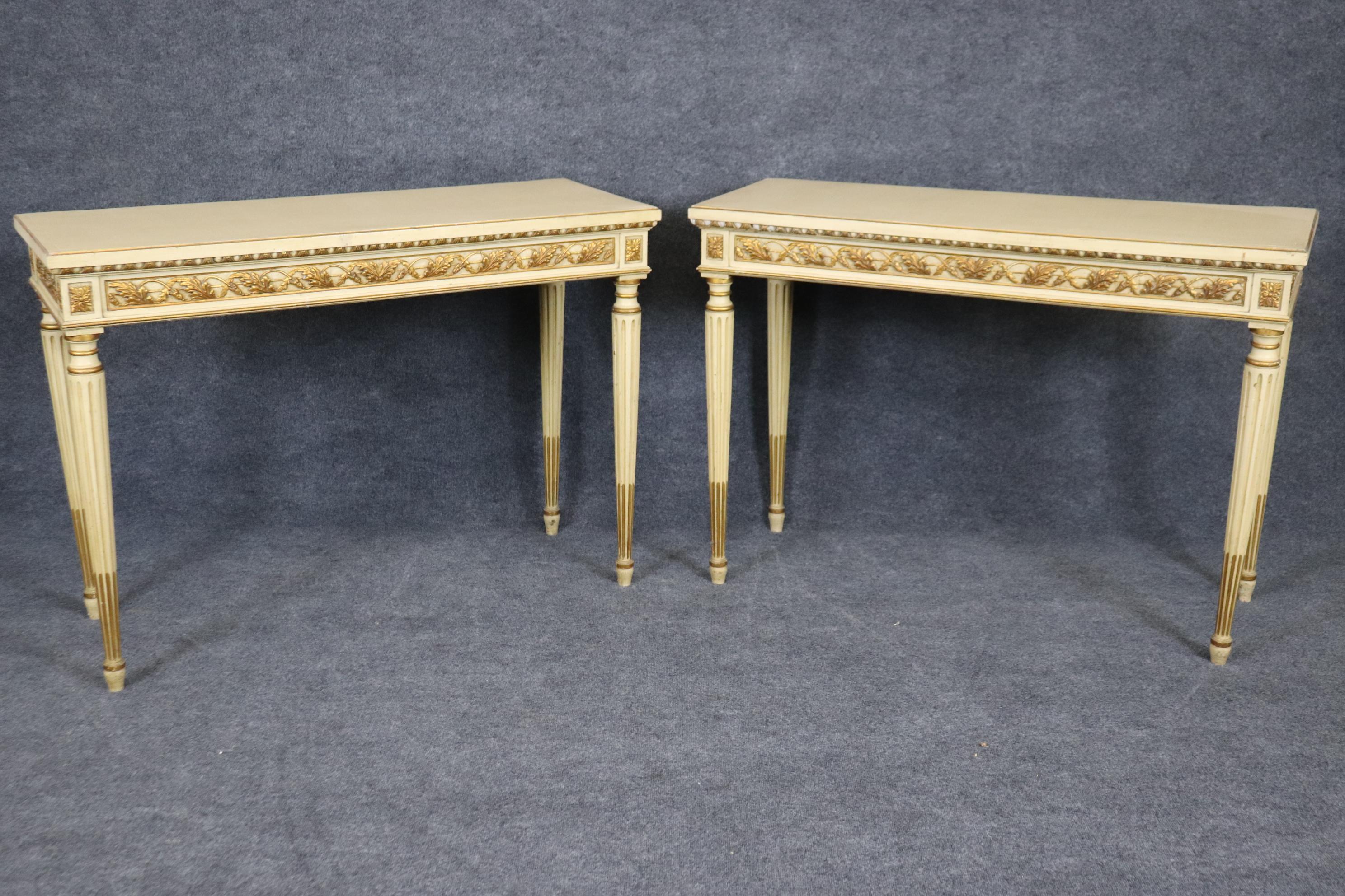 This is a beautiful pair of creme painted and gilded console tables with beautiful carved details like floral sprays and stop-fluted tapered legs. The tables are in good vintage condition and will shows signs of age such as minor chips in the