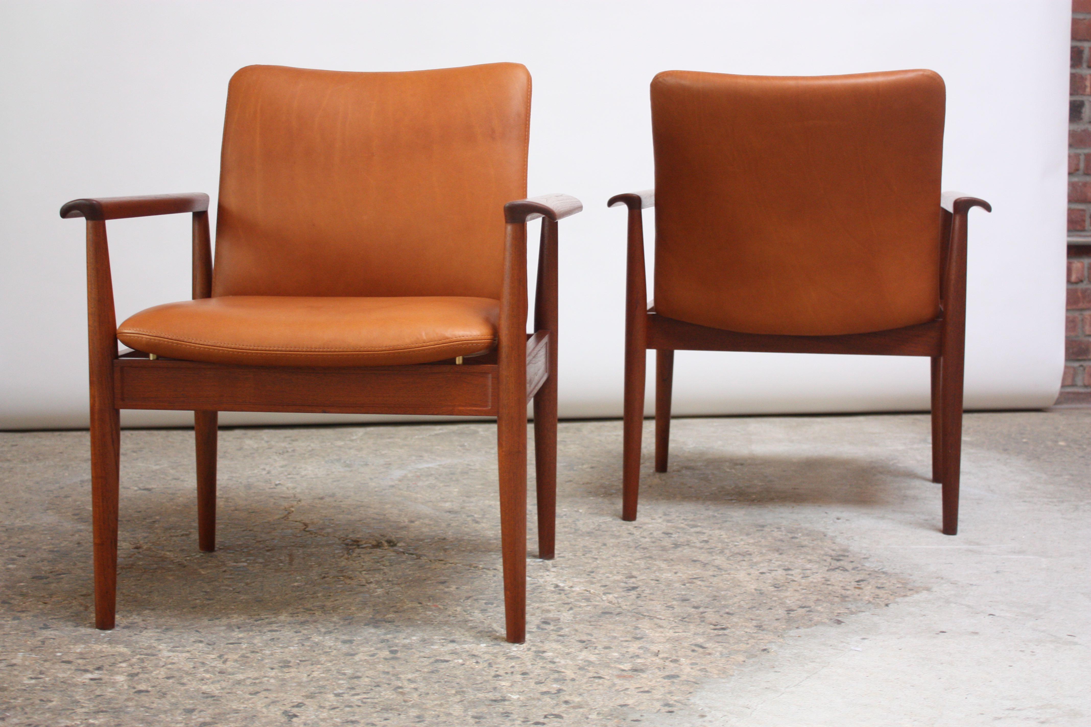 These teak 'Diplomat Chairs' were designed by Finn Juhl for France & Son circa 1961 and feature deeply sculpted arms and clean lines throughout. Leather seats mount to brass posts which connect to the frame, giving the chairs a floating