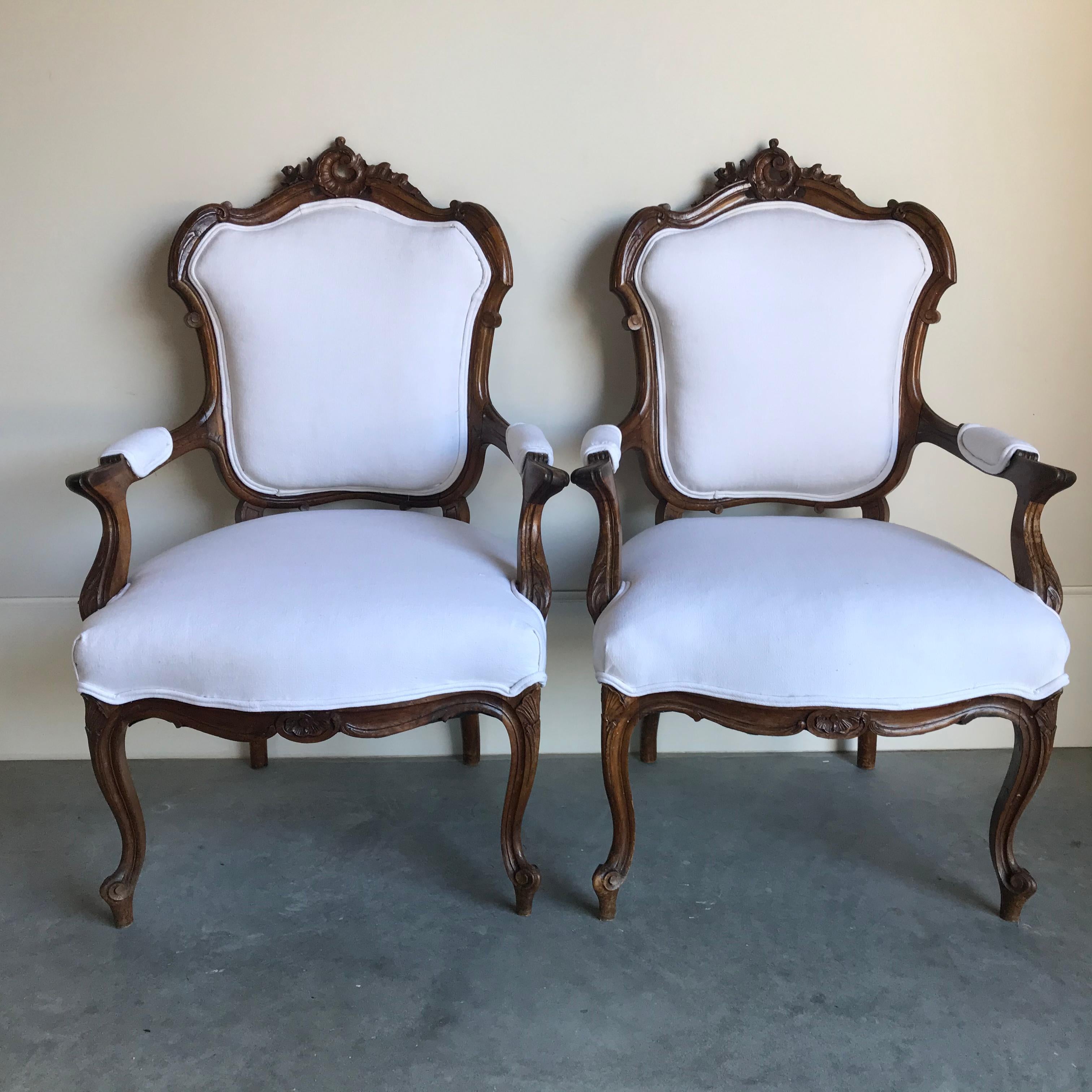 Two elegant Louis XV intricately carved walnut fauteuils or armchairs on cabriole legs decorated with hand carved seashell patterns. The arched back of the chair features delicately carved seashells and scrolls, and the wood armchairs are newly