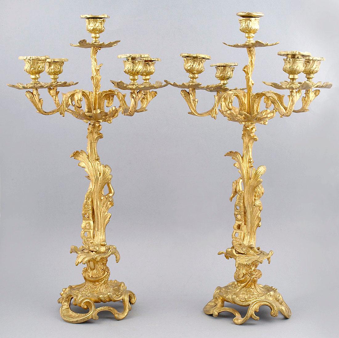 A pair of five-candle candelabra with an openwork, circular-shaped base with elements of shells and flowers with rocaille elements. Four arms extending to the sides and one extending above in the center of the candlestick. Each of the arms is bent,