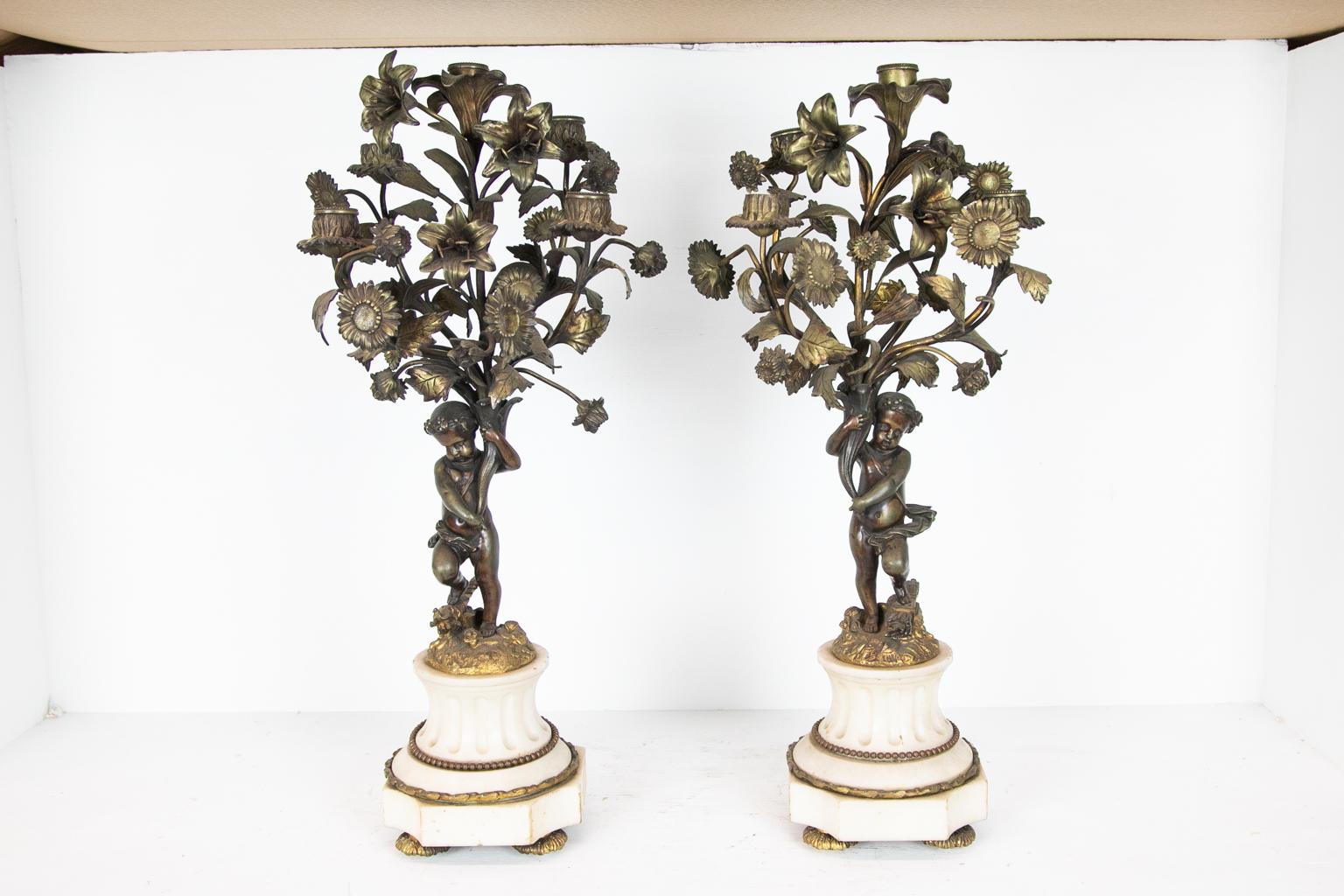 Pair of five hole cupid candelabra, the bases are white fluted marble with ormolu moldings and feet. The cupids are standing on quivers and torches while holding floral branches. The gilding is mostly worn down to the bronze metal.
  