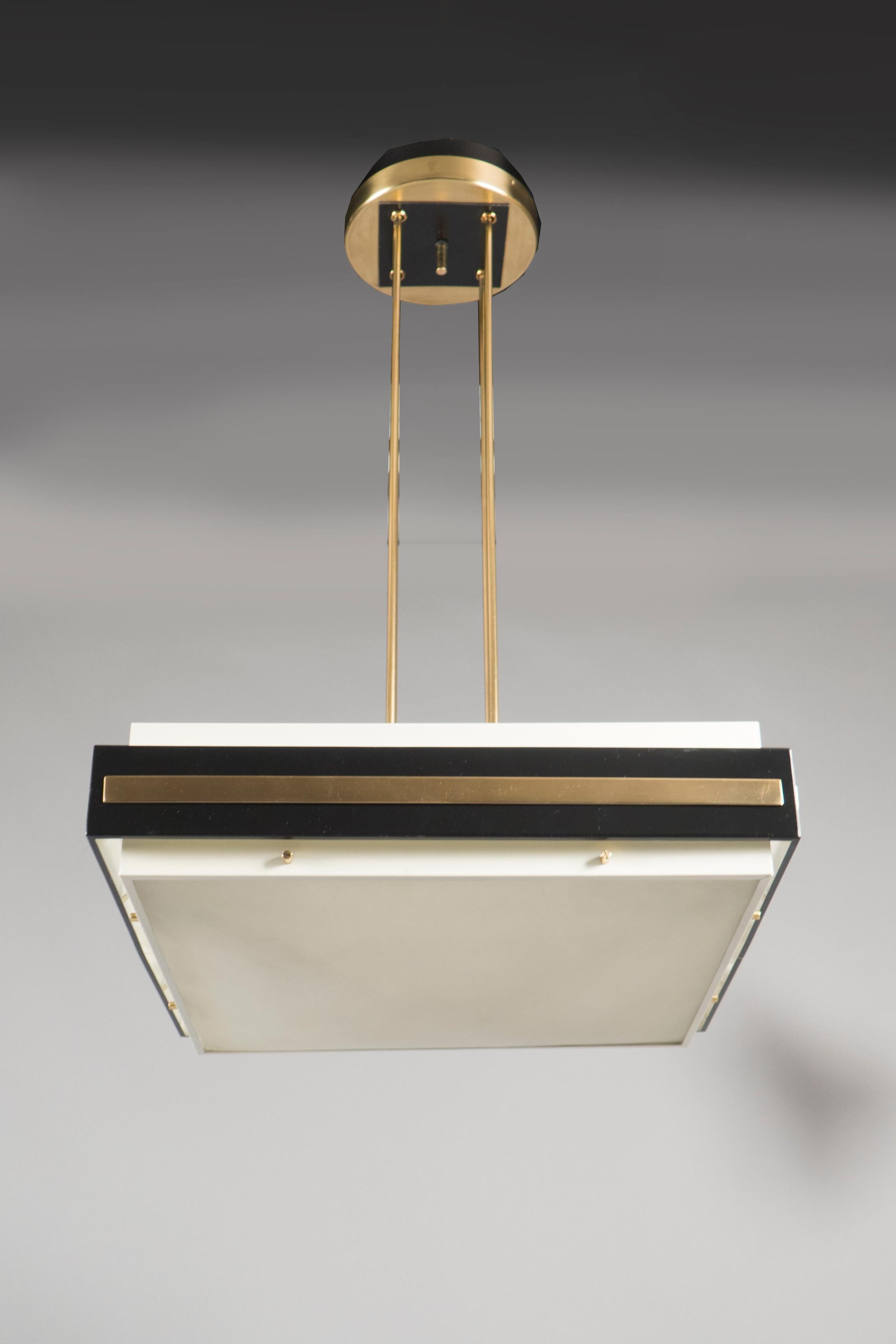 Black painted and polished brass structures, each consisting of a square squat body with acid etched glass diffusers, suspended from four polished brass rods. Original sticker.