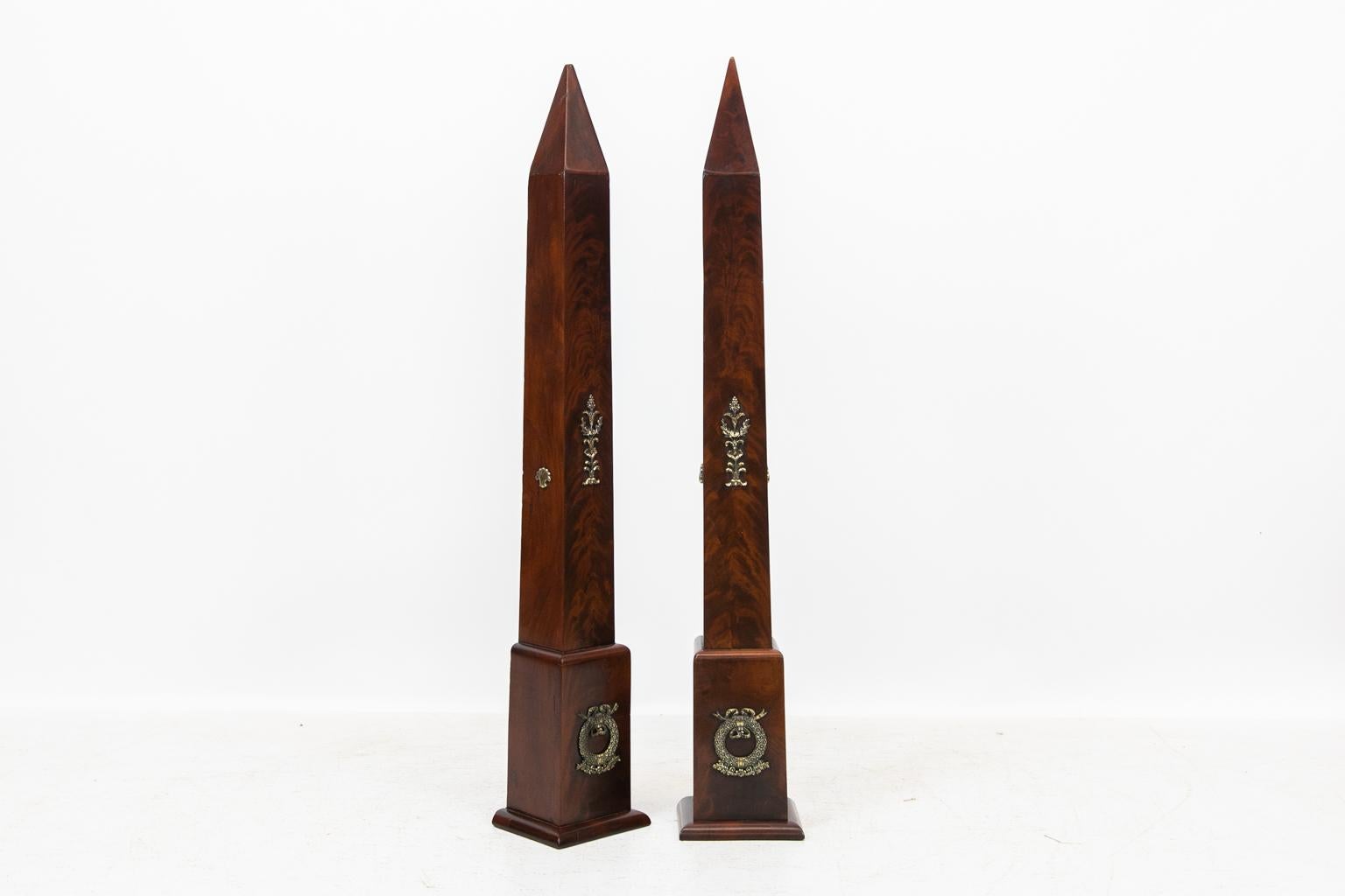 Pair of flame grained mahogany obelisks, with heavy cast brass wreaths, scallop shells, and floral castings.
  
