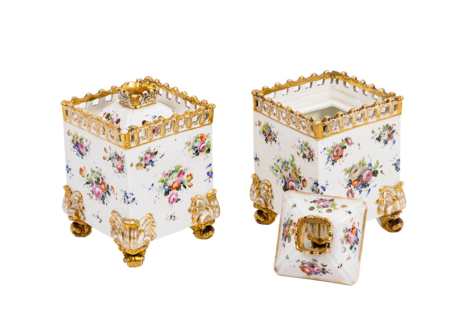 Pair of tiny square flasks in porcelain of Paris. Adorned with bouquets of flowers and acanthus leaves on each inferior angle. Pyramidal cover drilled in its center. Top shaped as a gilt railing. It stands on four foliage scroll legs.

Work