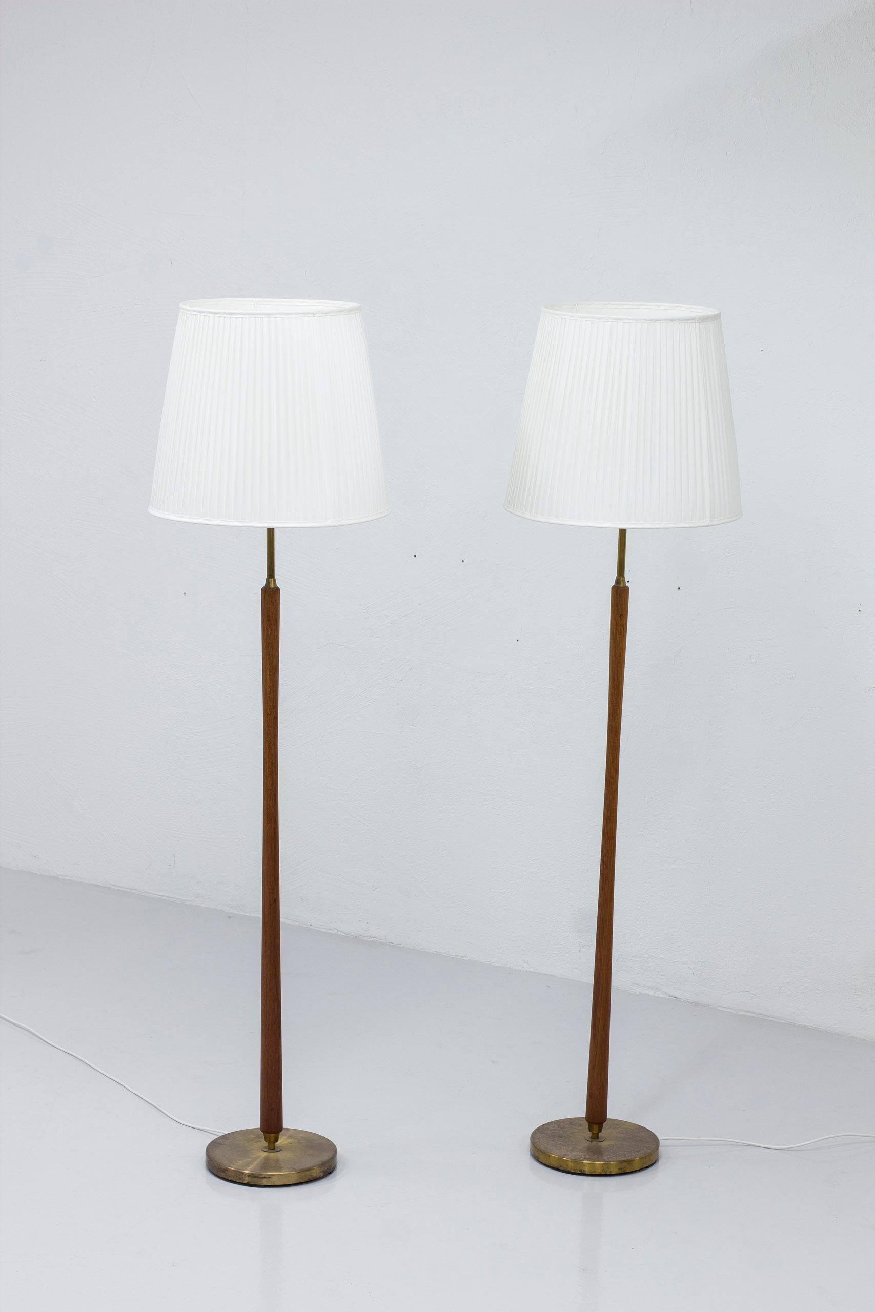 Pair of floor lamps produced in Sweden by ASEA belysning. Made from solid brass and teak stems with a nice concave shape. New lamp shades in hand sewn chintz fabric with single pleating, matching the aluminum uplight fixture. The fixture makes it