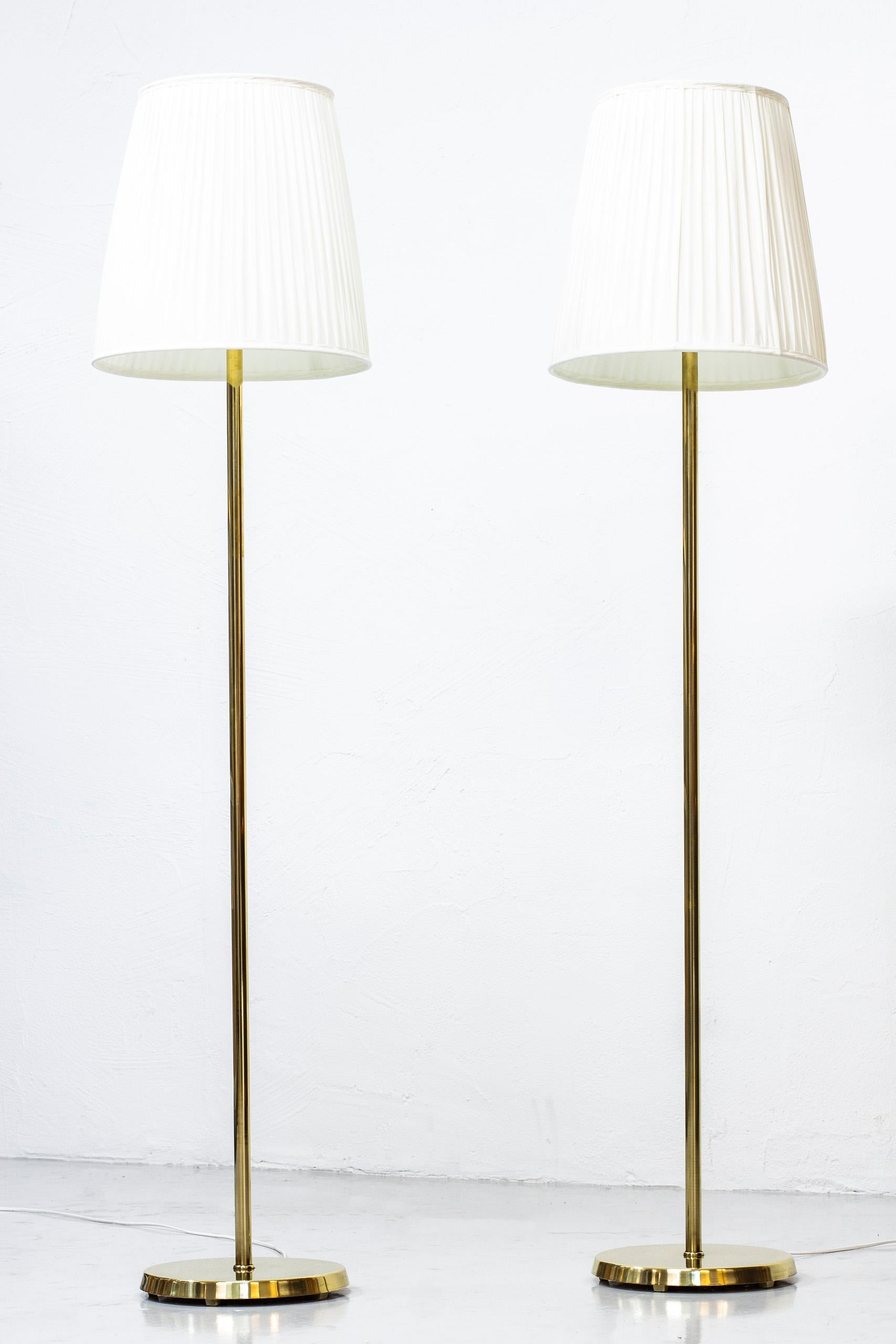 Pair of floor lamps produced in Sweden by ASEA Belysning during the 1950s. Made from solid polished brass, with opaline inner glass and chintz fabric shades. Light switch on the lamp fixture in working order. Very good vintage condition with light