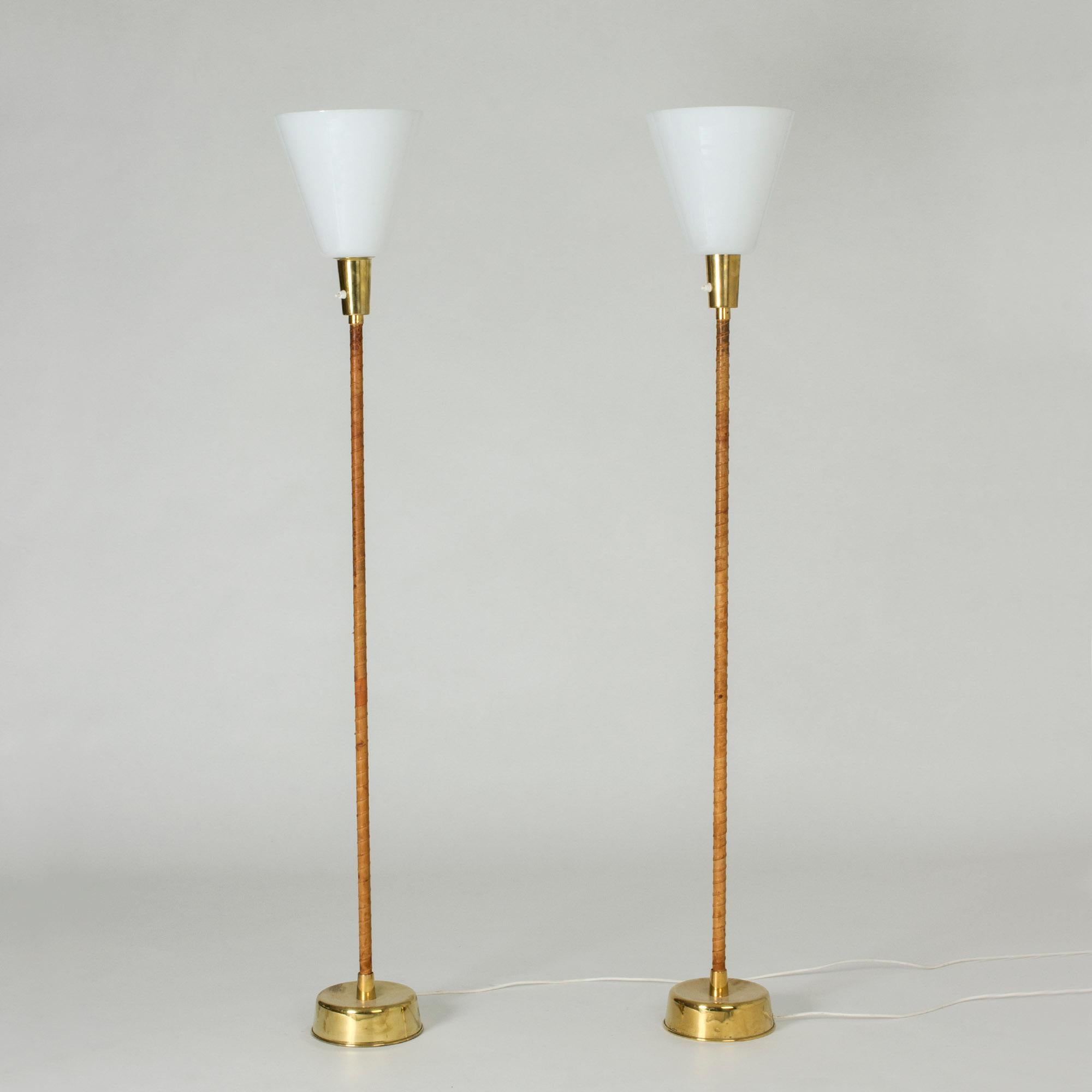 Ein Paar Stehlampen von Lisa Johansson-Pape, die durch ihre Schlichtheit bestechen. Sockel aus Messing und umwickelte Griffe aus braunem Leder, voluminöse weiße Lampenschirme. Die Schirme lassen sich leicht abnehmen, um die Lampen in Stehleuchten