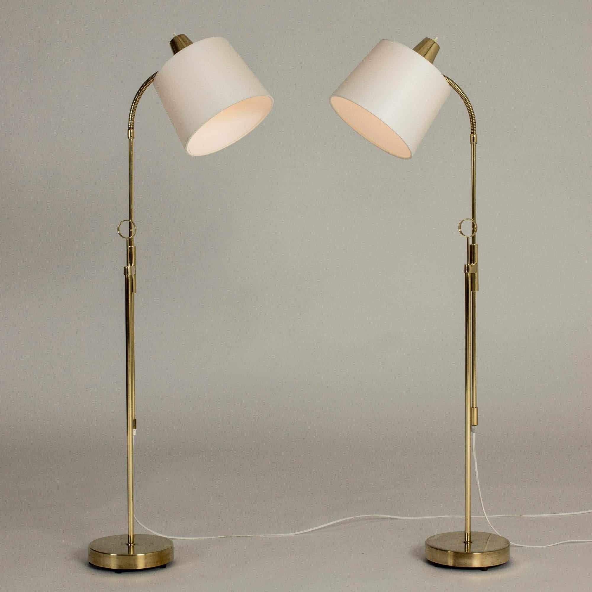 Pair of elegant brass floor lamps from Falkenbergs Belysning, with adjustable height. Hoops on the stems make a decorative detail as well as having a practical use.
