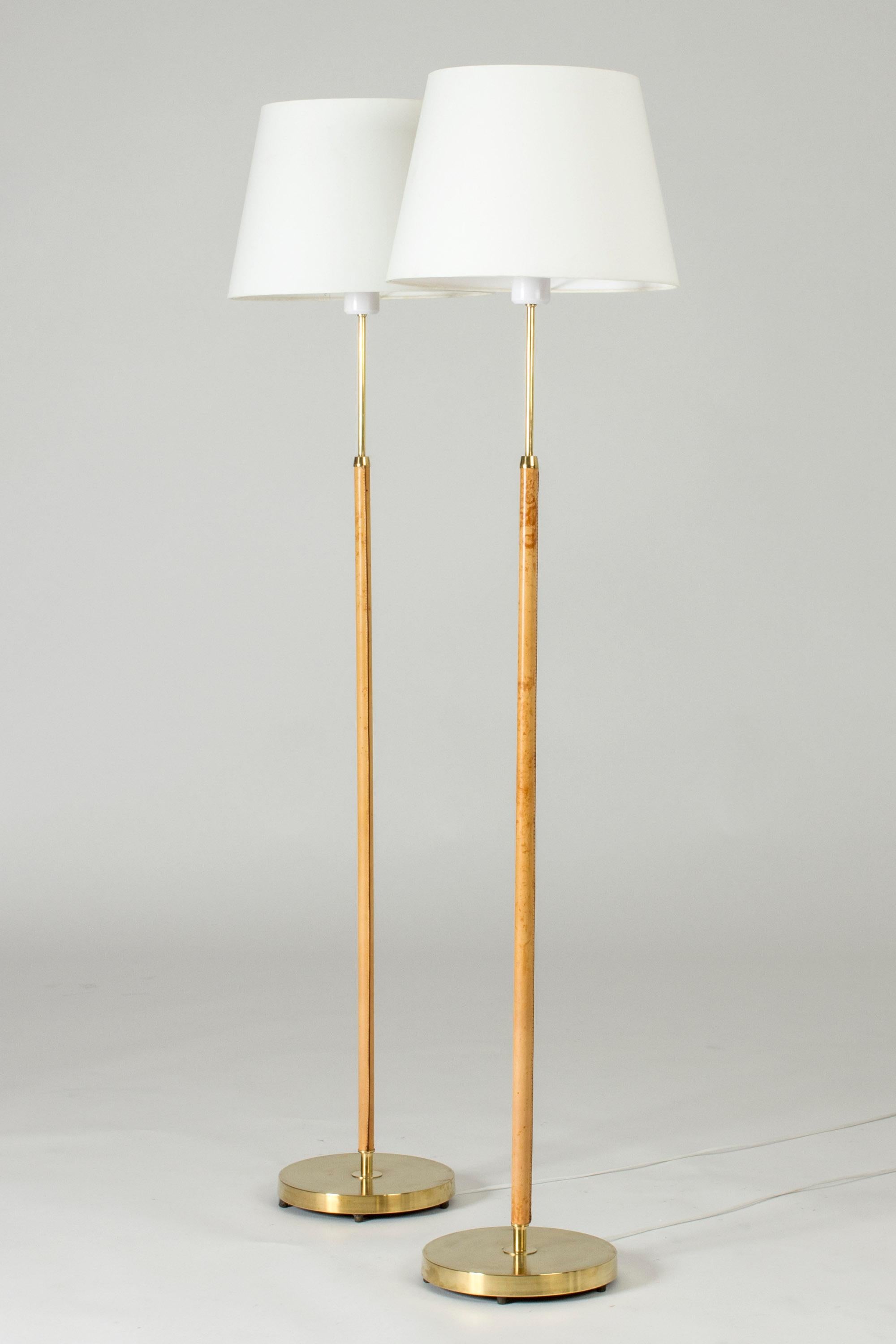 Pair of elegant floor lamps from Falkenbergs Belysning, made from brass. Sleek stems dressed with nicely patinated nude leather, decorative white seams.