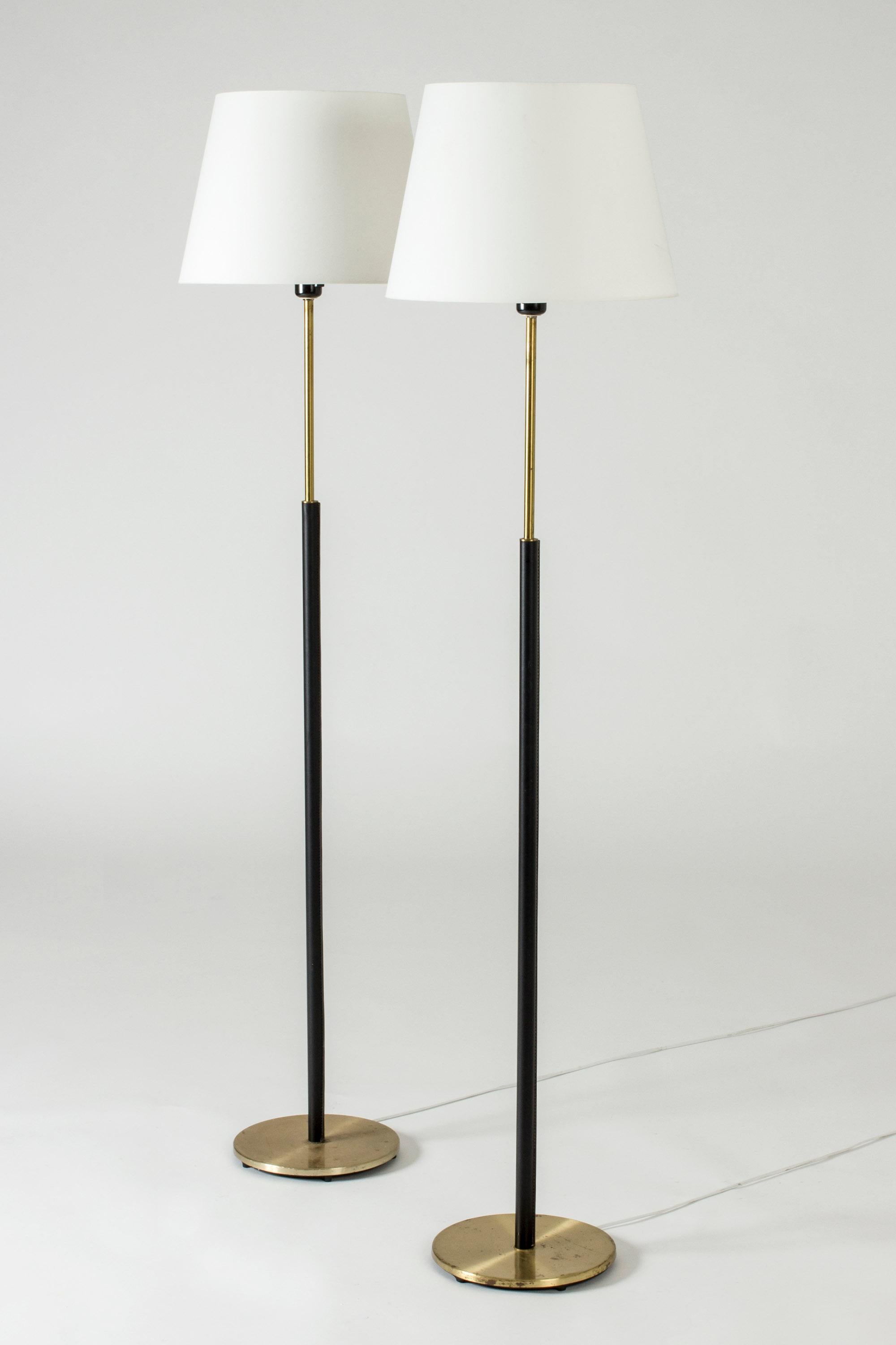 Pair of elegant floor lamps from Falkenbergs Belysning, made from brass. Sleek stems dressed with black leather, decorative white seams.