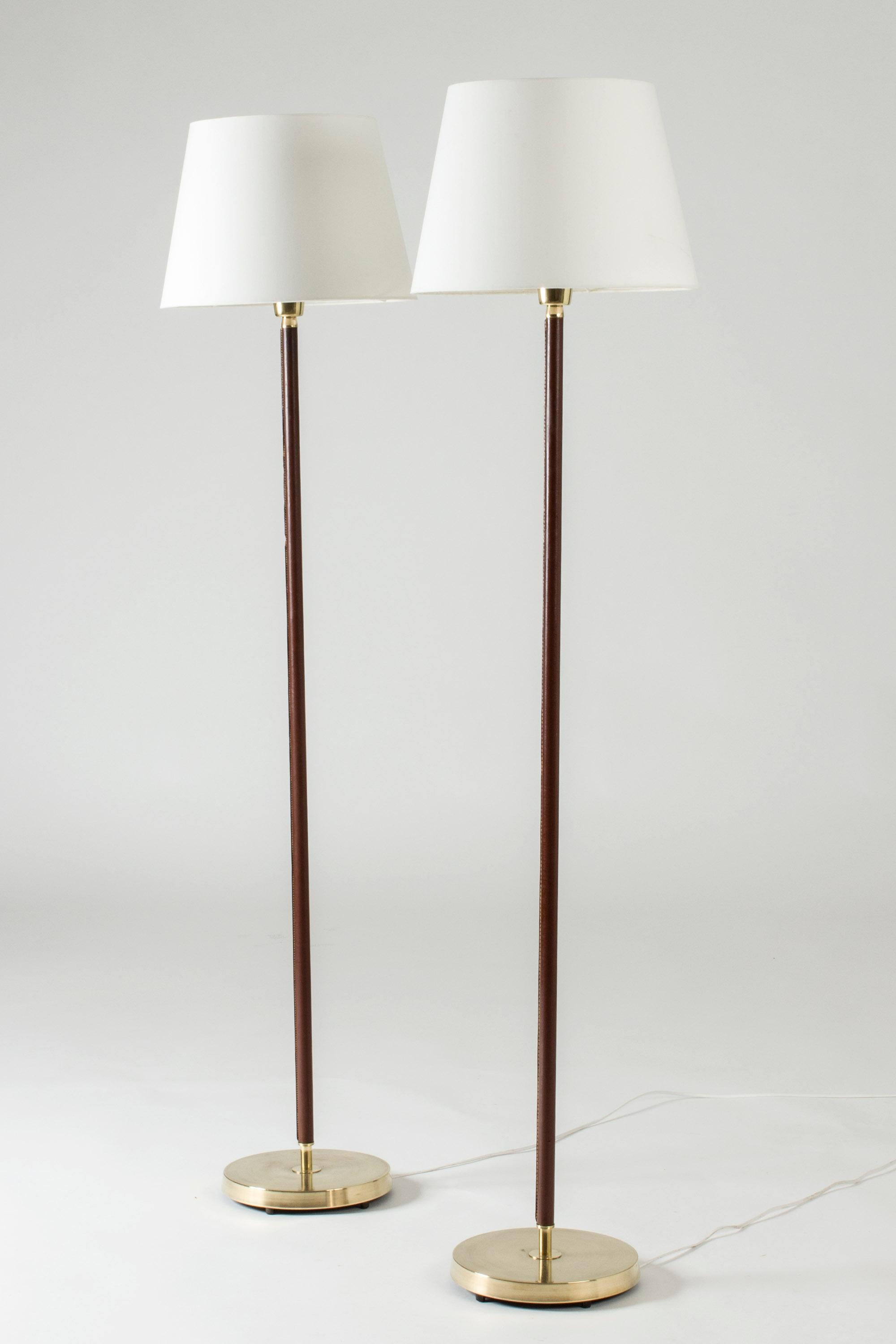 Pair of elegant floor lamps from Falkenbergs Belysning, made from brass. Sleek stems dressed with brown leather, decorative white seams.