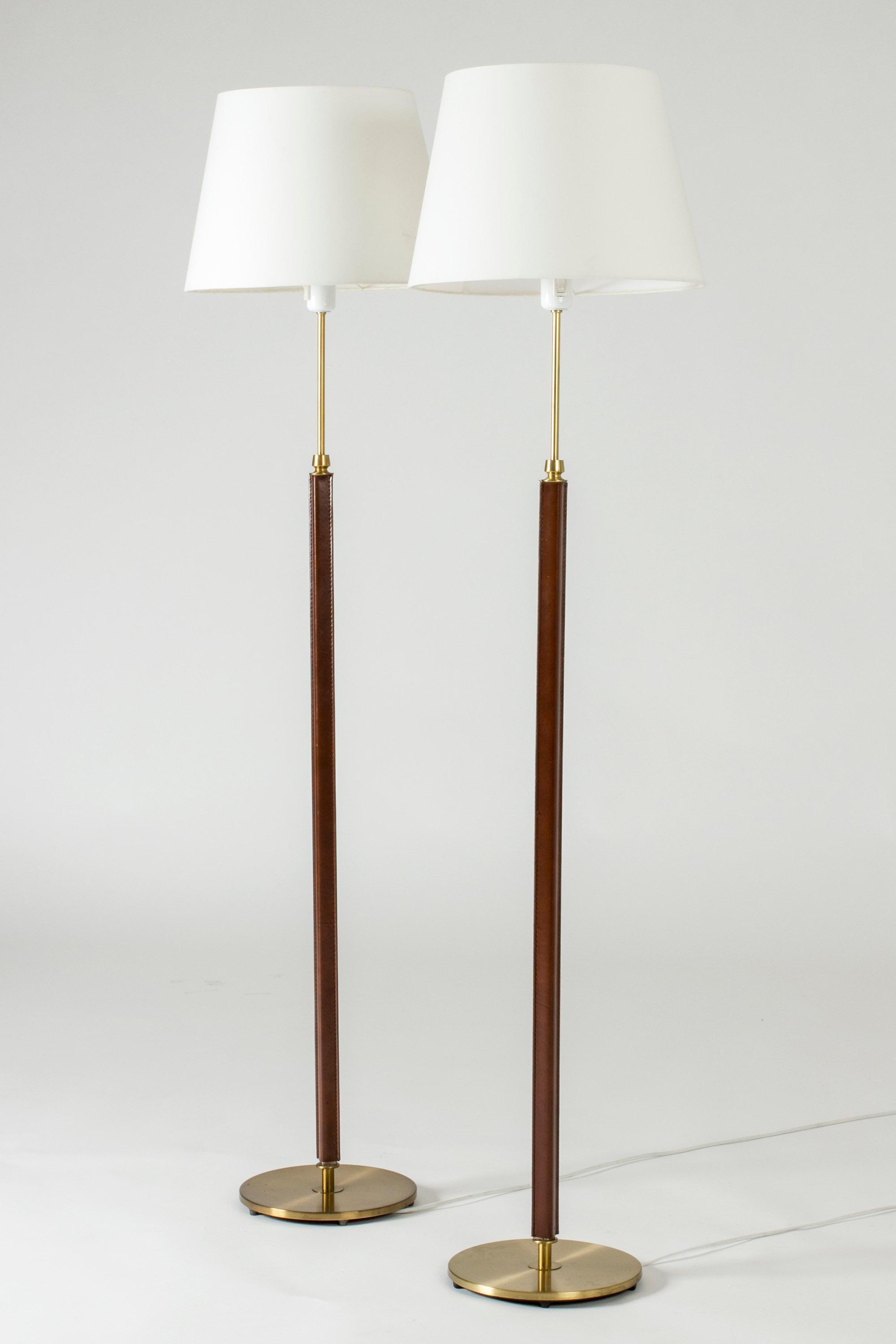 Pair of cool floor lamps from Falkenbergs Belysning, made from brass. Sleek square stems dressed with brown leather.