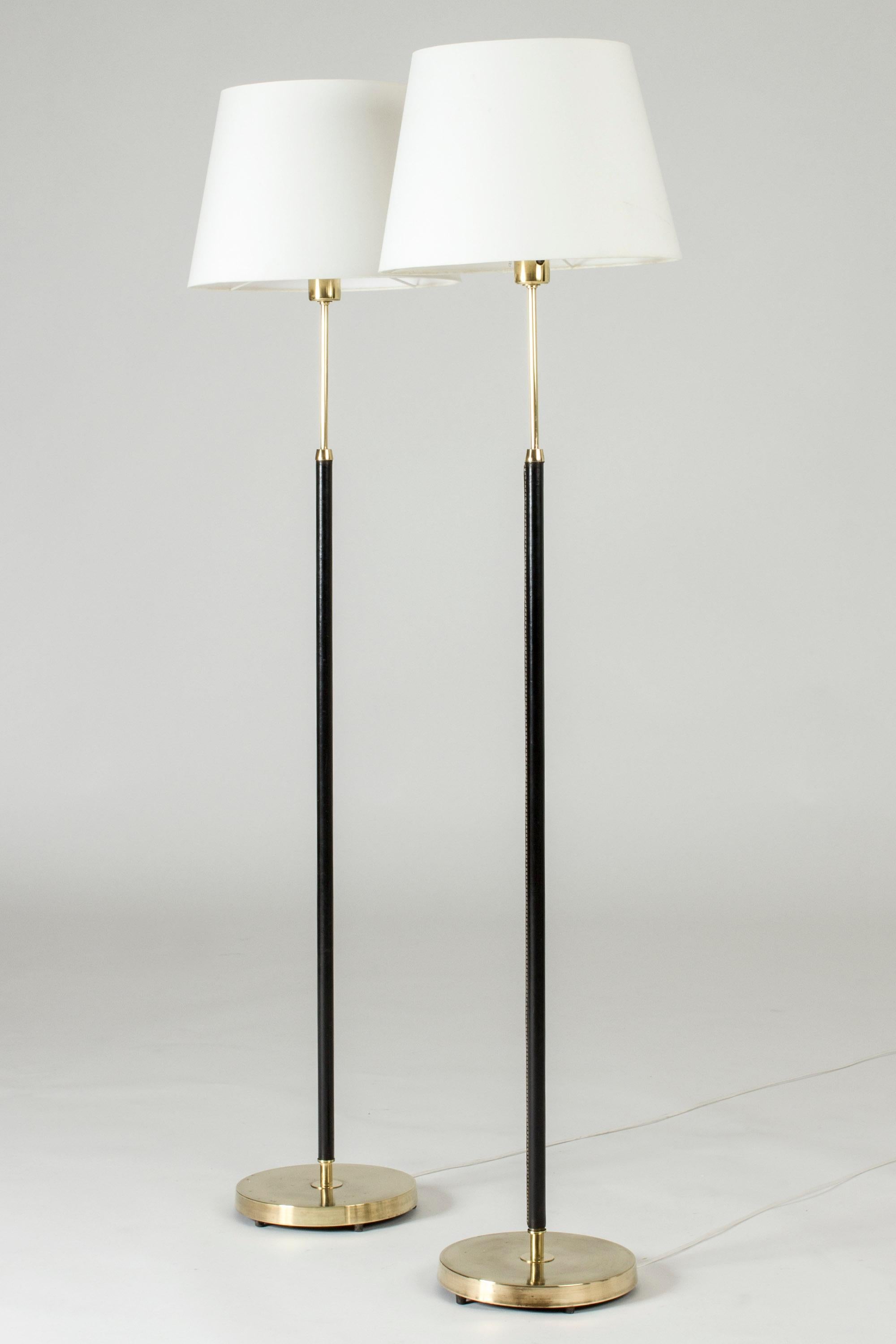 Pair of elegant floor lamps from Falkenbergs Belysning, made from brass. Sleek stems dressed with black leather, decorative white seams.