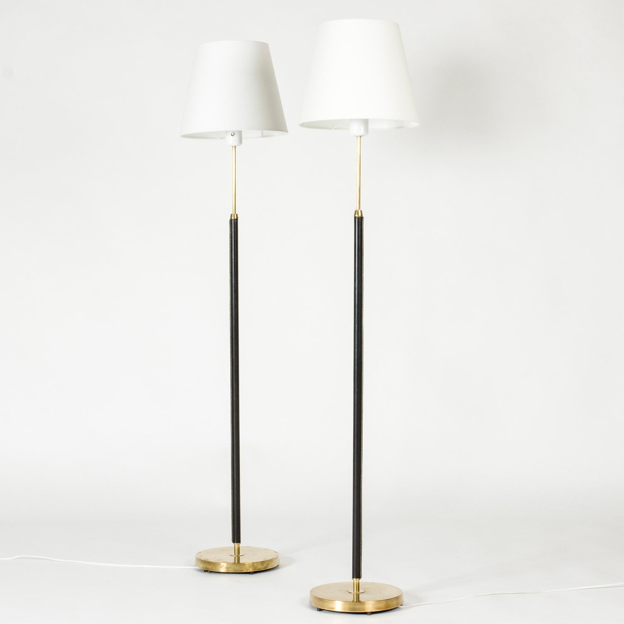 Pair of elegant floor lamps from Falkenbergs Belysning, made from brass. Sleek stems dressed with black leather, decorative white seams.