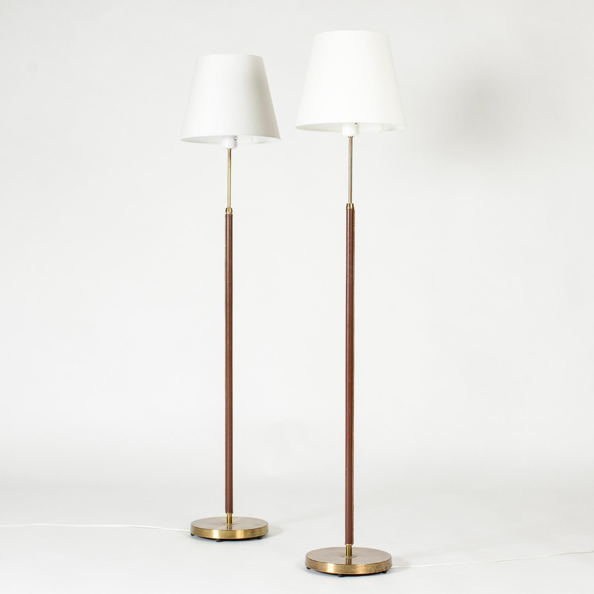 Pair of elegant floor lamps from Falkenbergs Belysning, made from brass. Sleek stems dressed with reddish brown leather, decorative white seams.