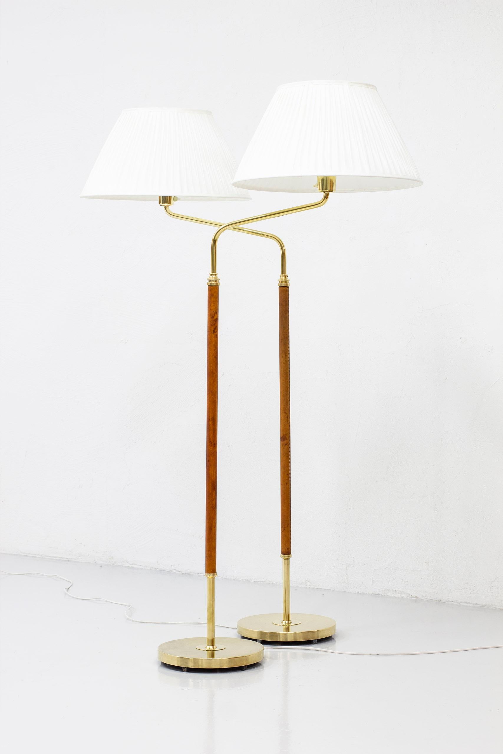 Pair of floor lamps model 31644 designed by Bertil Brisborg. Produced by Nordiska Kompaniet from 1947-1950s. Made from brass, cast iron and with original cognac colored leather. New creme colored chintz shade with hand sewn pleating. Light switch on