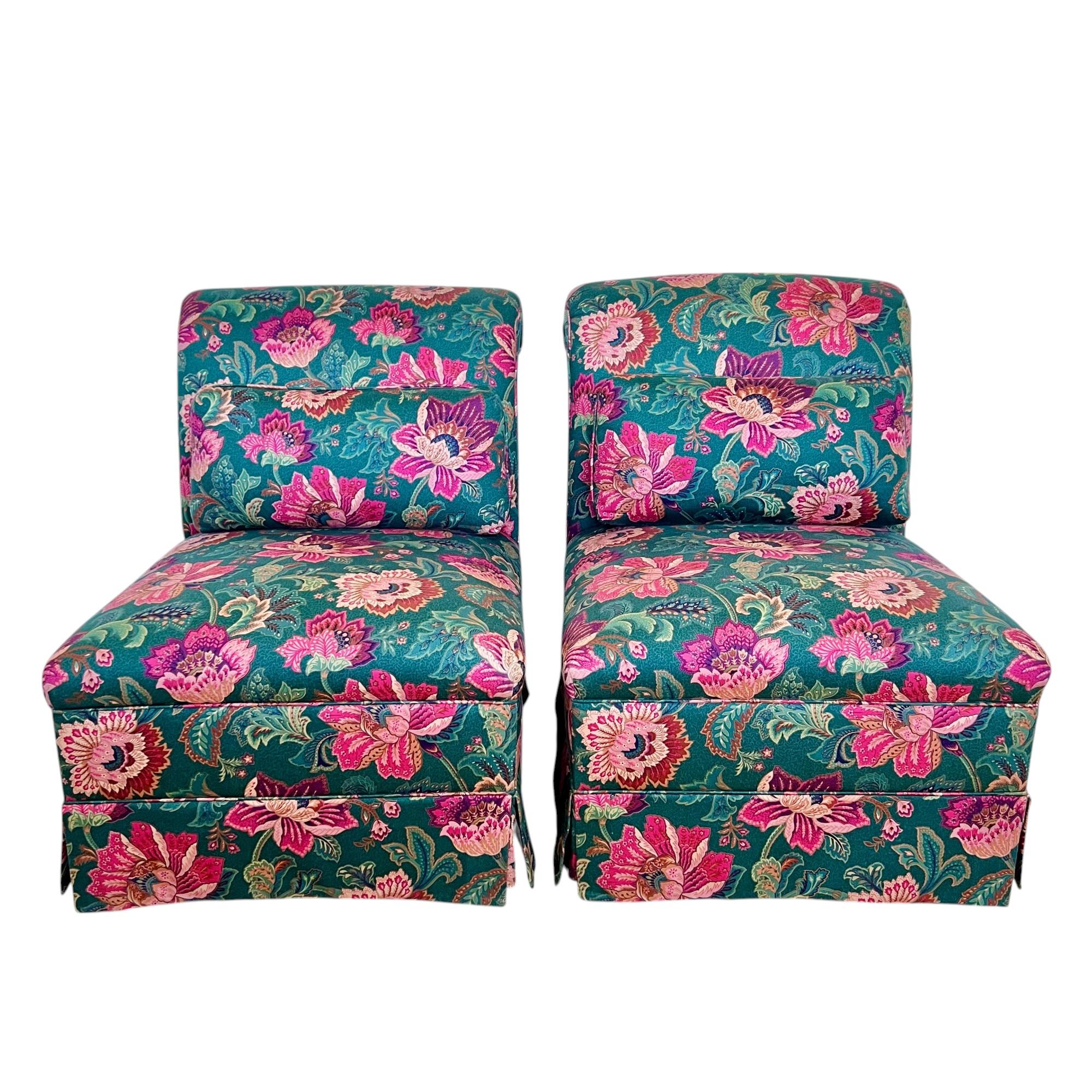 A vintage pair of slipper chairs featuring rolled backs, floral design fabric and skirts over tapered wood legs with gliders. These lovely seats are upholstered in a medium weight polished cotton in vibrant shades of green, pink, purple and peach.