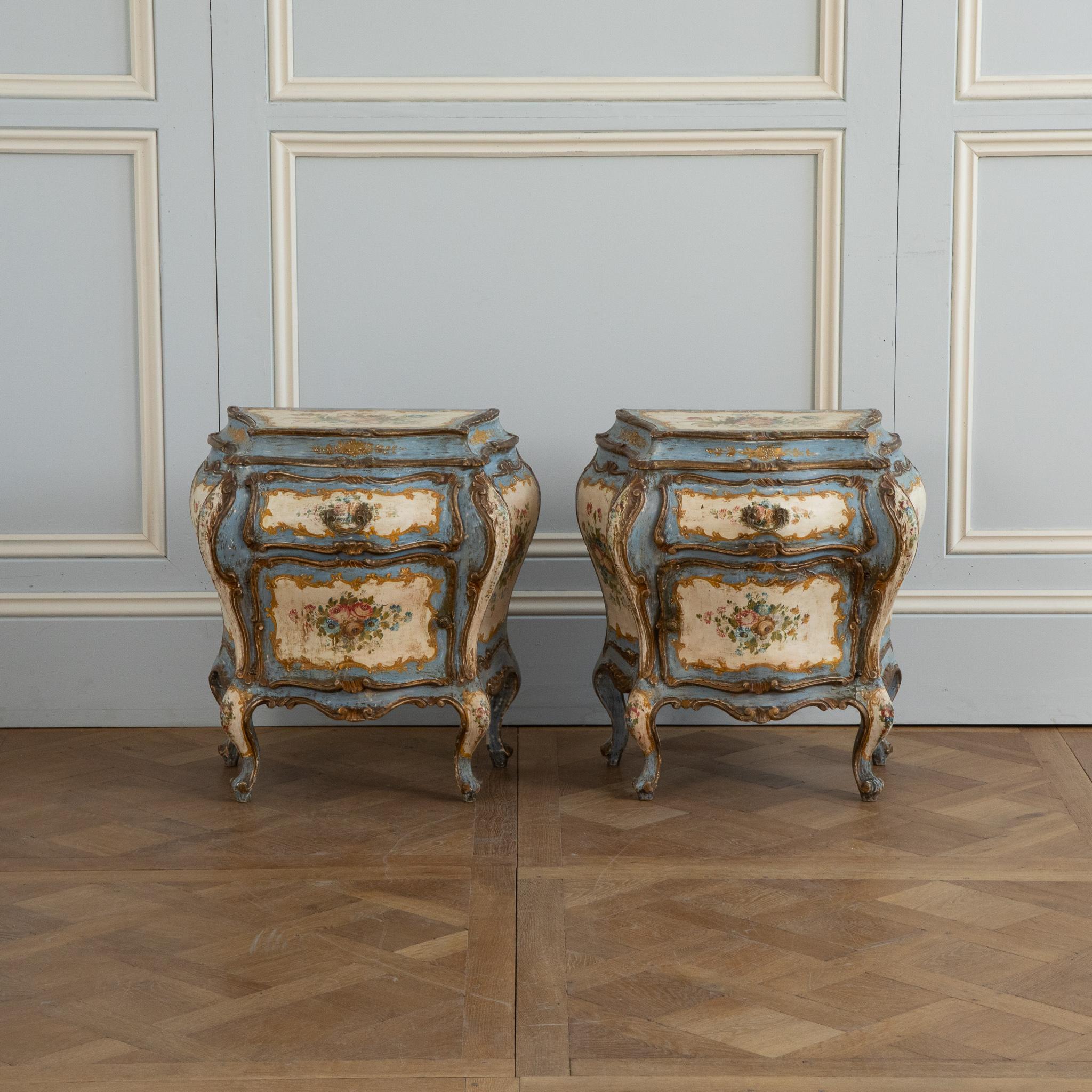 A vivacious Rococo style Tuscanian Pair of bombe Night stands or Bedside tables from the early 1900's, hand painted with delicate floral motifs on the main colours of old white and cobalt blue with gilded highlights.