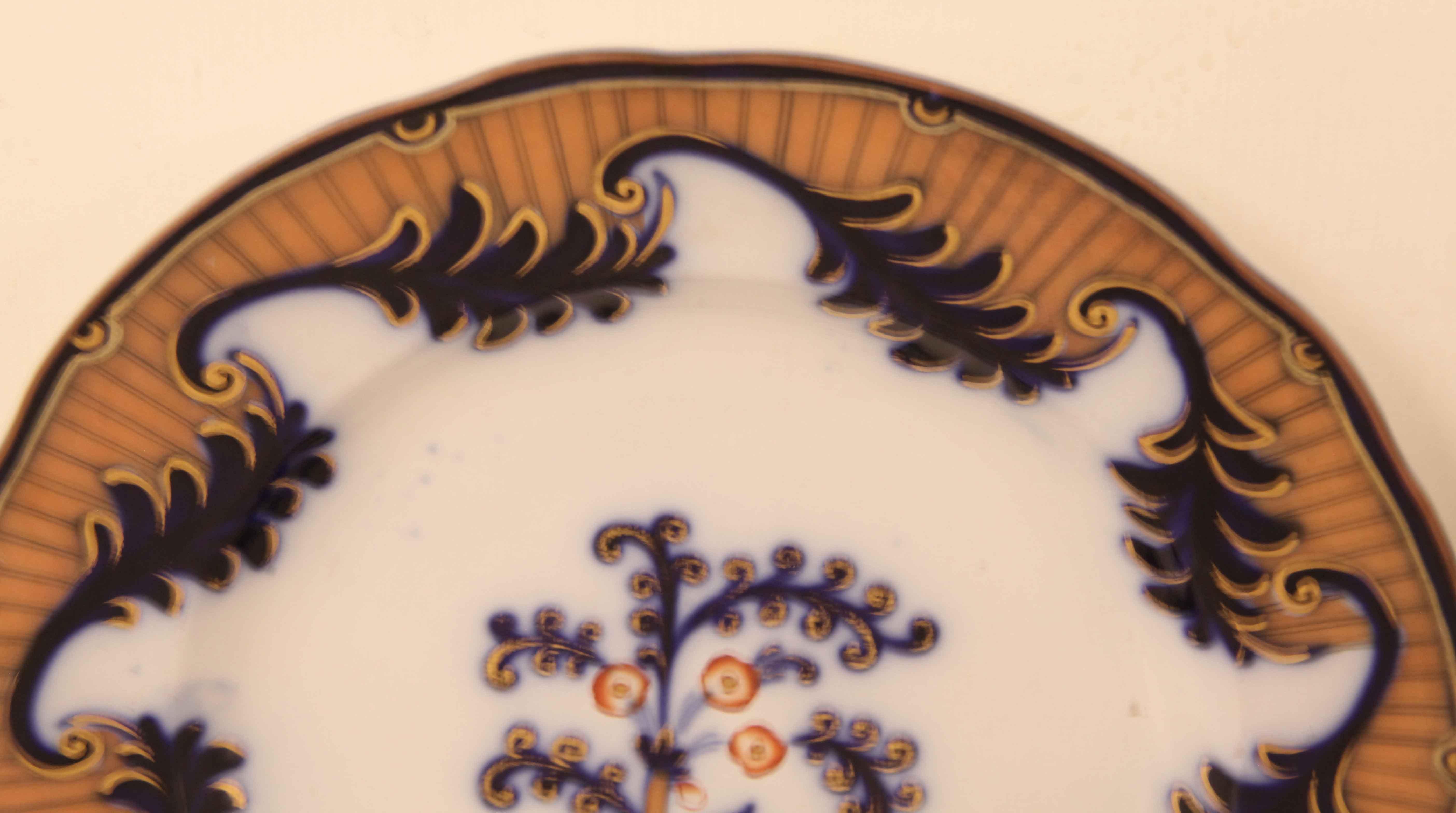 Pair of flow blue Staffordshire plates, the border features a repeating pattern of stylized leaves with gilt edges connected with volutes, this is inside a coral colored background with double straight pin lines around the perimeter.  The main body