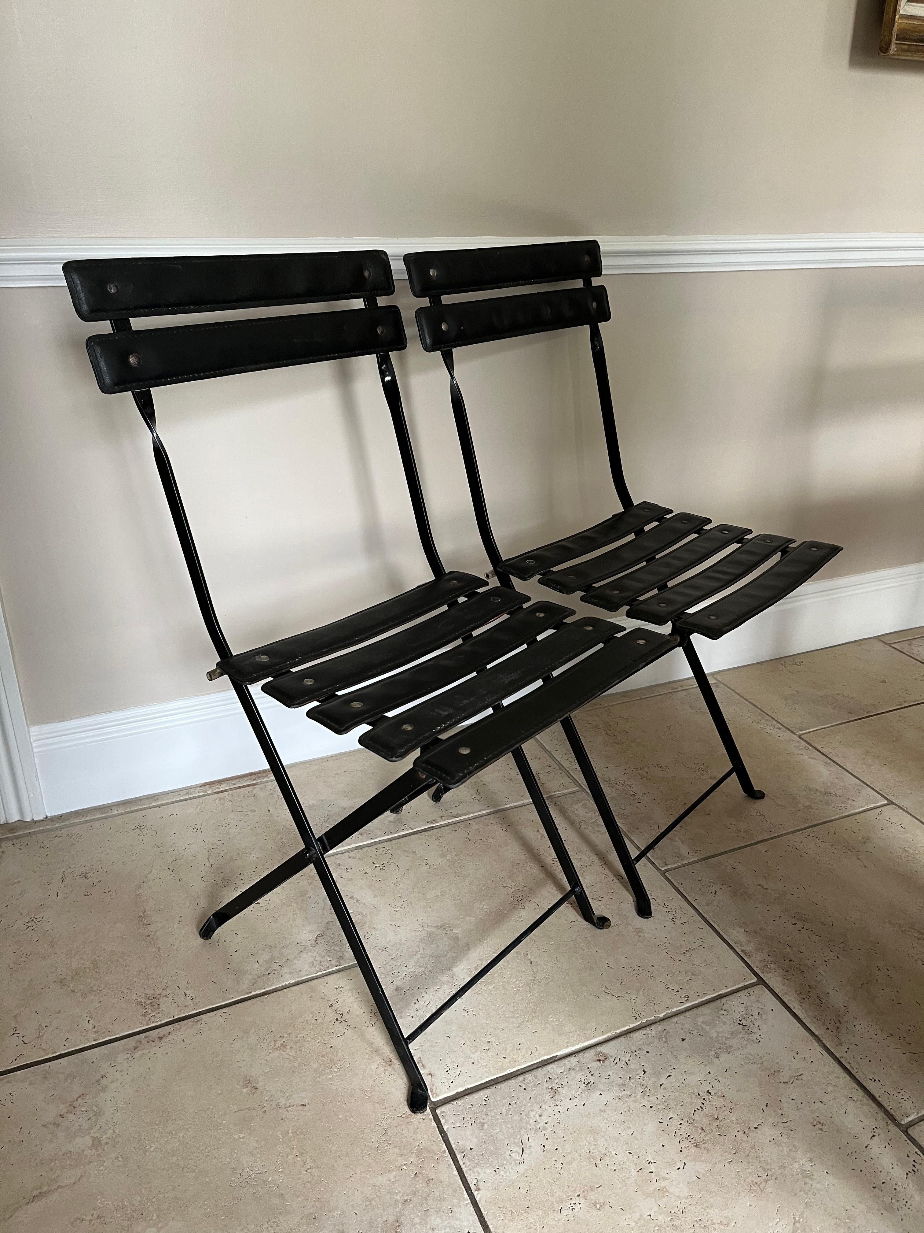 A pair of faux leather and black metal folding chairs attributed to Jacques Adnet. Elegant pair of useful side chairs. Steel rivets, some wear and tear but still attractive and useable.