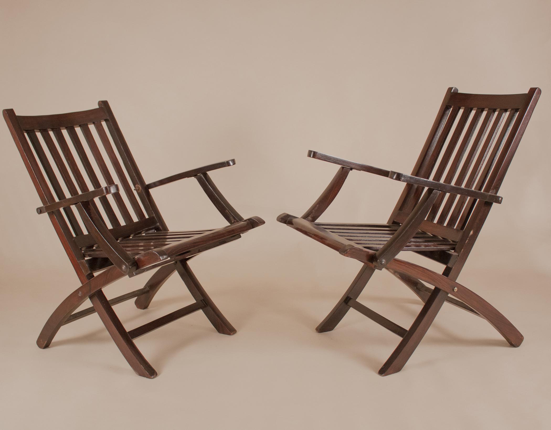 A pair of folding British steamer chairs that evokes the romance of a 1940s ship's voyage across the Indian Ocean. As stylish as they are practical, these portable deck chairs have gorgeous lines and are crafted from richly refinished rosewood. The