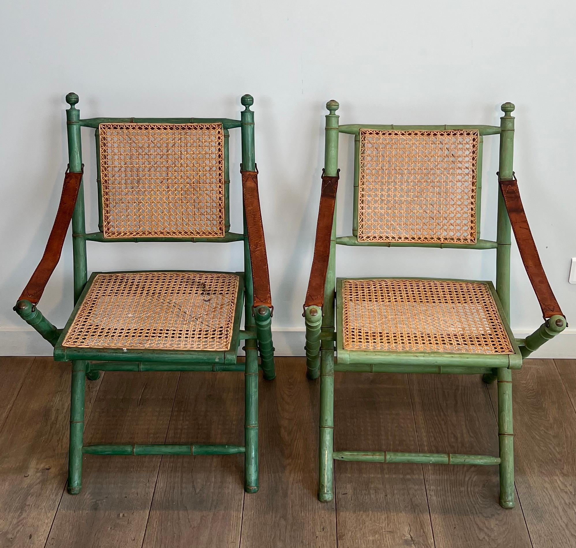This nice and unusual pair of folding Safari chairs are made of patinated faux bamboo with caned backs and seats and leather armrests. This is a French work. Circa 1970