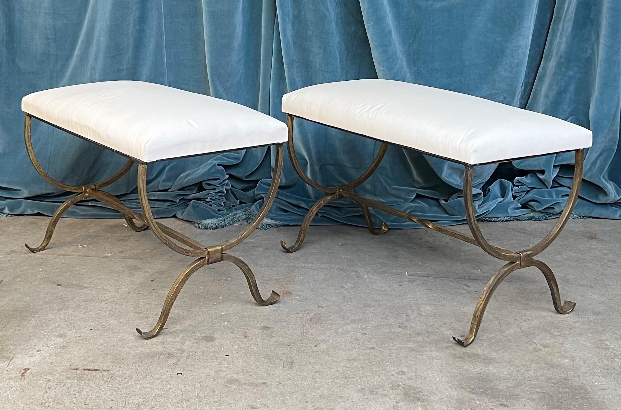 An elegant pair of recently made iron benches with scrolled legs and upholstered in a plain muslin fabric.  Handmade by expert European craftsmen, this pair of benches have hand forged iron bases with a rich but subtle gold patinated finish