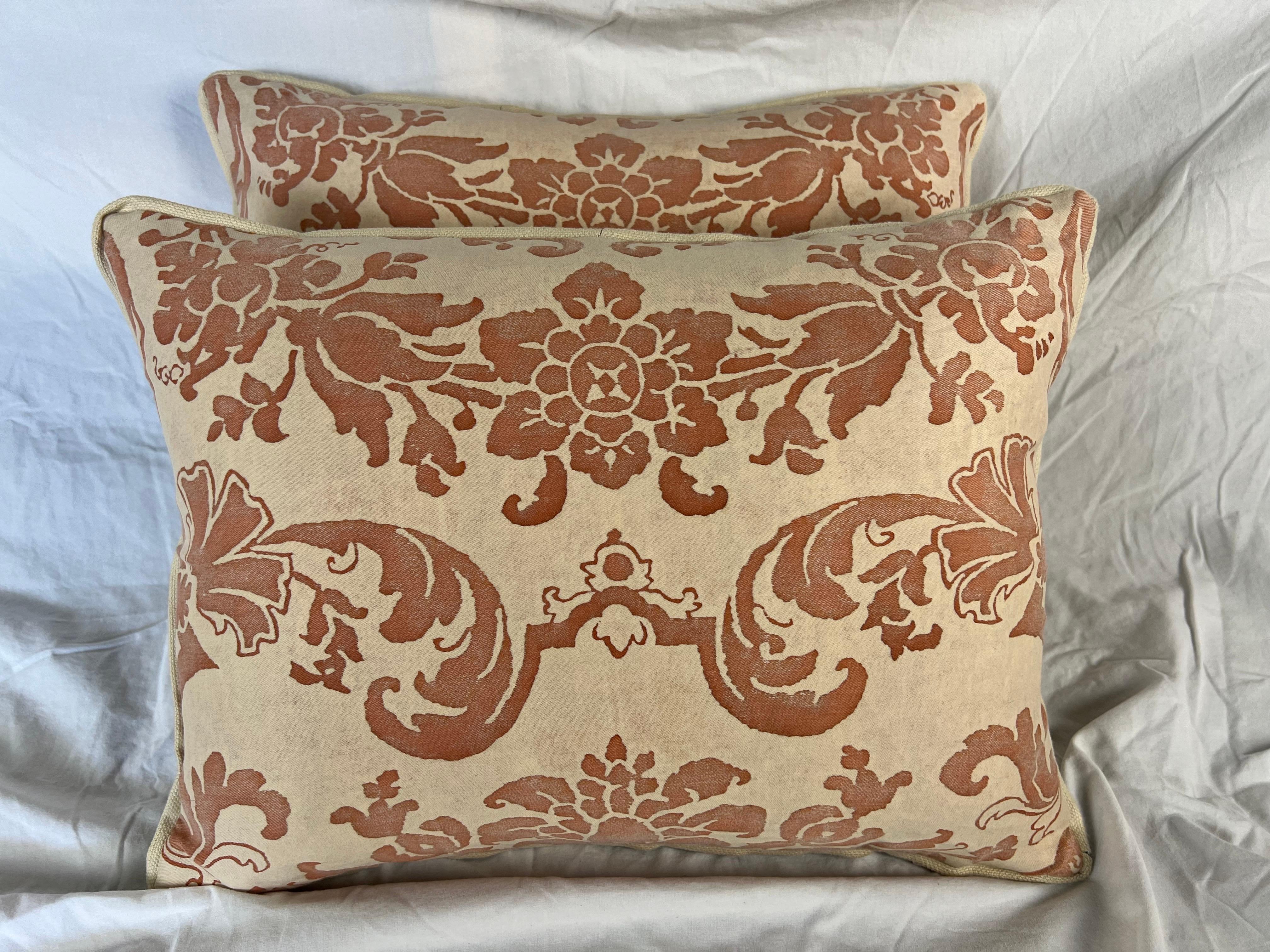 Questi eleganti cuscini sono realizzati con l'iconico tessuto Fortuny e presentano un classico motivo damascato in una calda tonalità di terracotta su un morbido sfondo beige. Il design presenta elementi floreali e fogliati stilizzati disposti in un