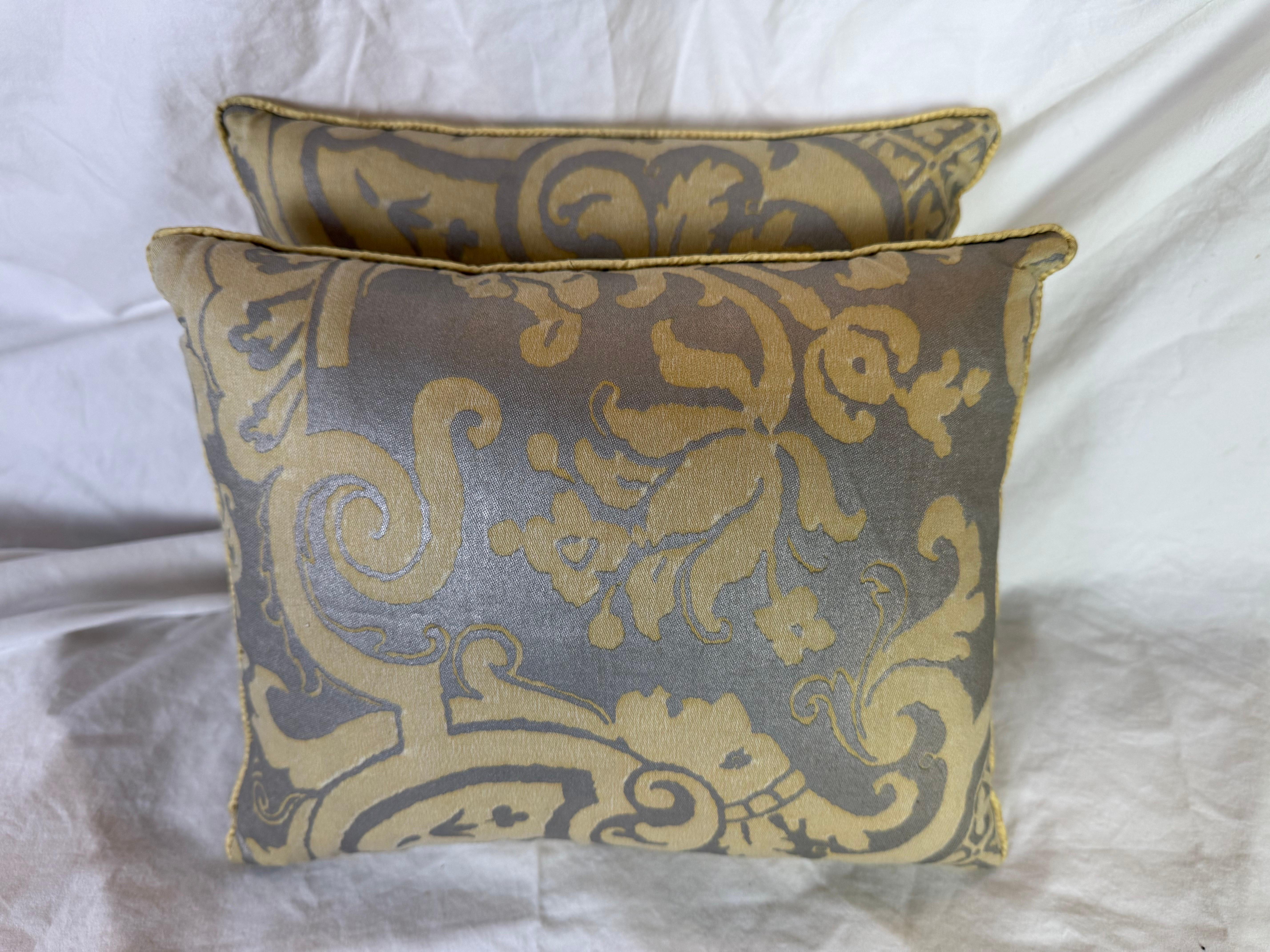 Ces coussins Fortuny présentent un design spectaculaire et royal avec des volutes baroques audacieuses et des éléments floraux. Le tissu présente un motif doré saisissant imprimé sur un fond gris argenté ou étain doux, ce qui donne un effet bicolore