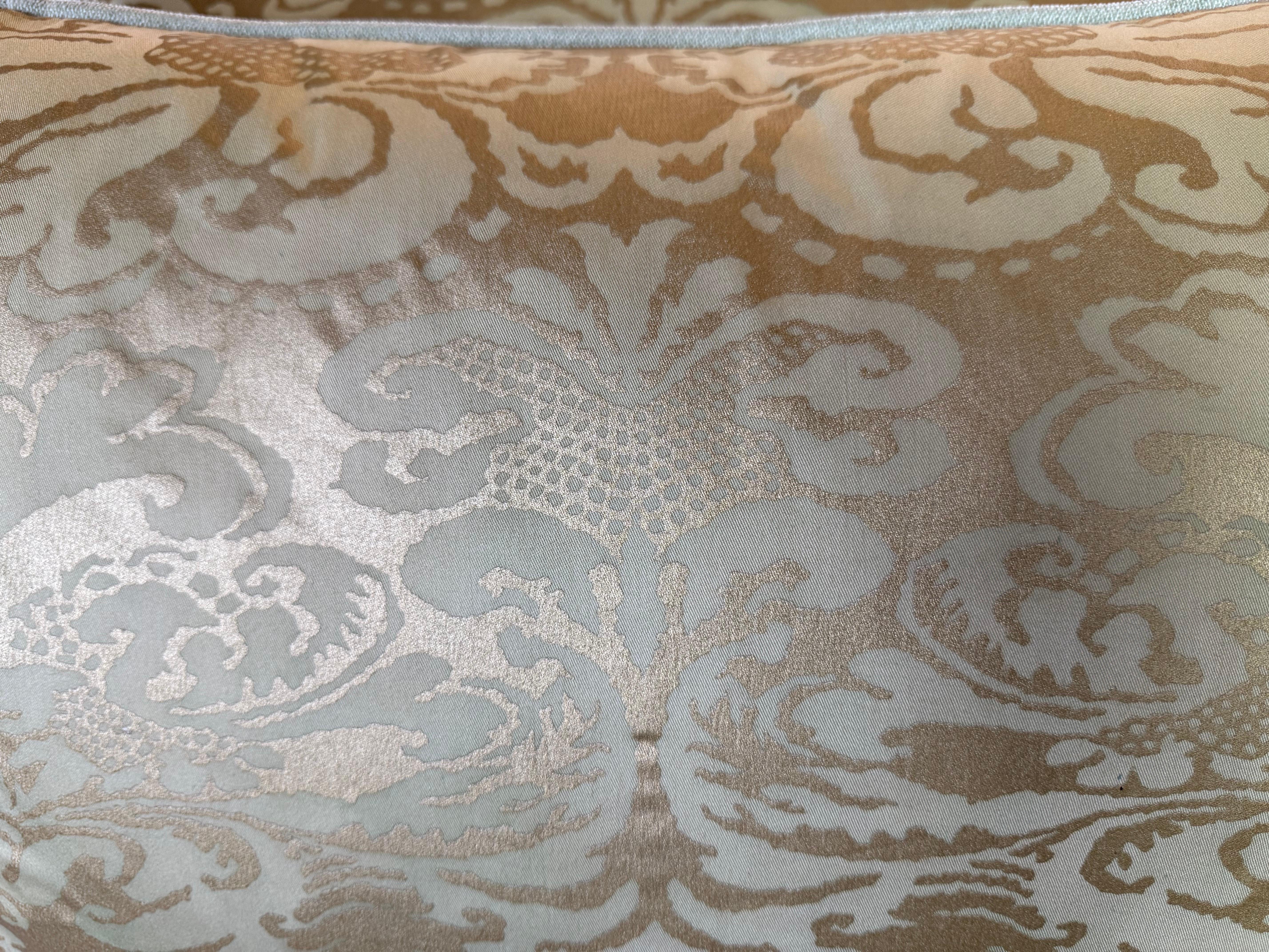 These are Fortuny textile pillows featuring a luxurious damask pattern in a muted gold and cream color scheme. The fabric showcases Fortuny’s signature intricate design, with elaborate floral and foliate motifs that have a slightly raised, luminous