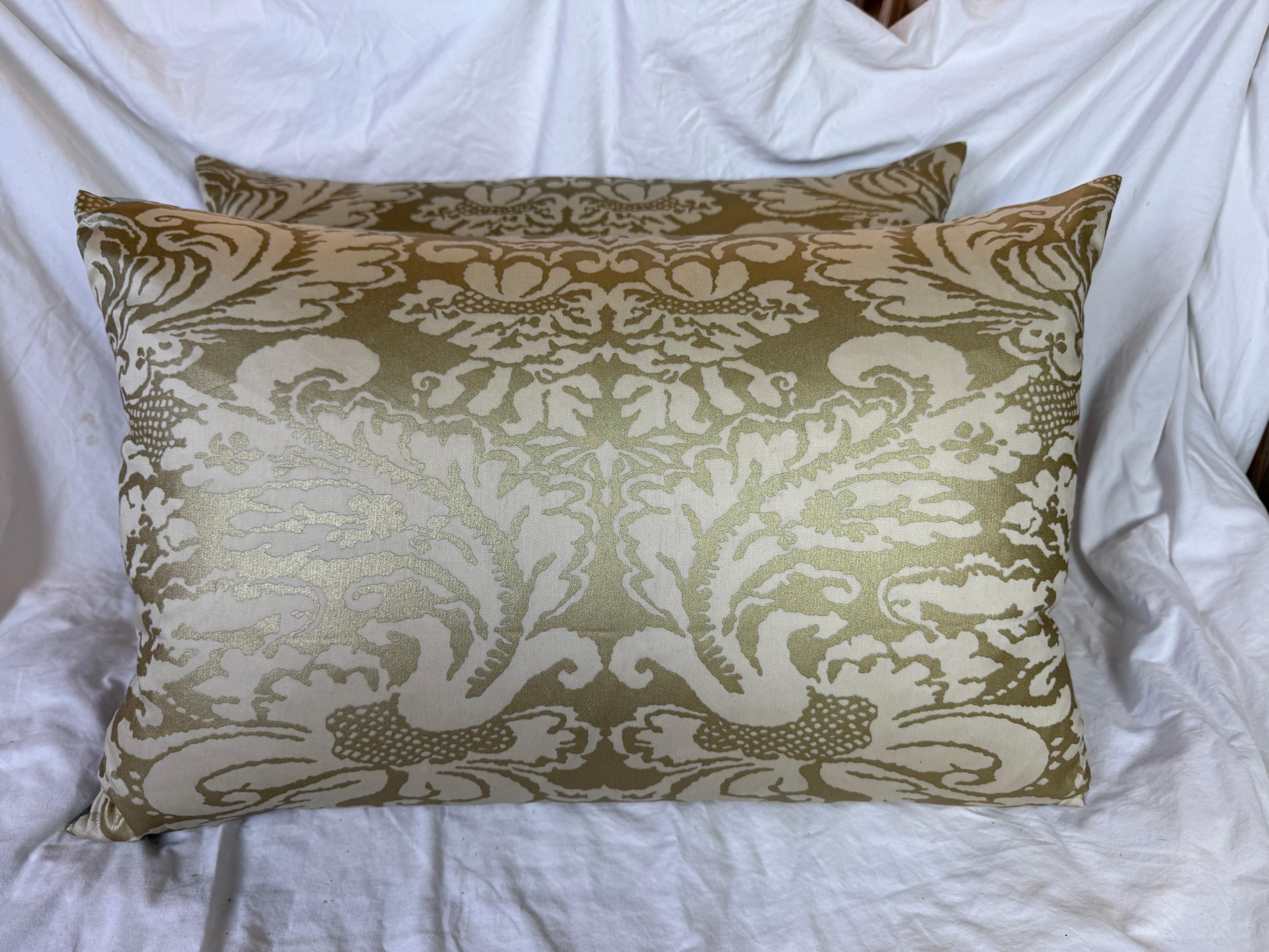 Questi cuscini in tessuto Fortuny presentano un lussuoso motivo damascato in una tenue combinazione di colori oro e crema. Il tessuto presenta l'intricato design tipico di Fortuny, con elaborati motivi floreali e fogliati che presentano una qualità