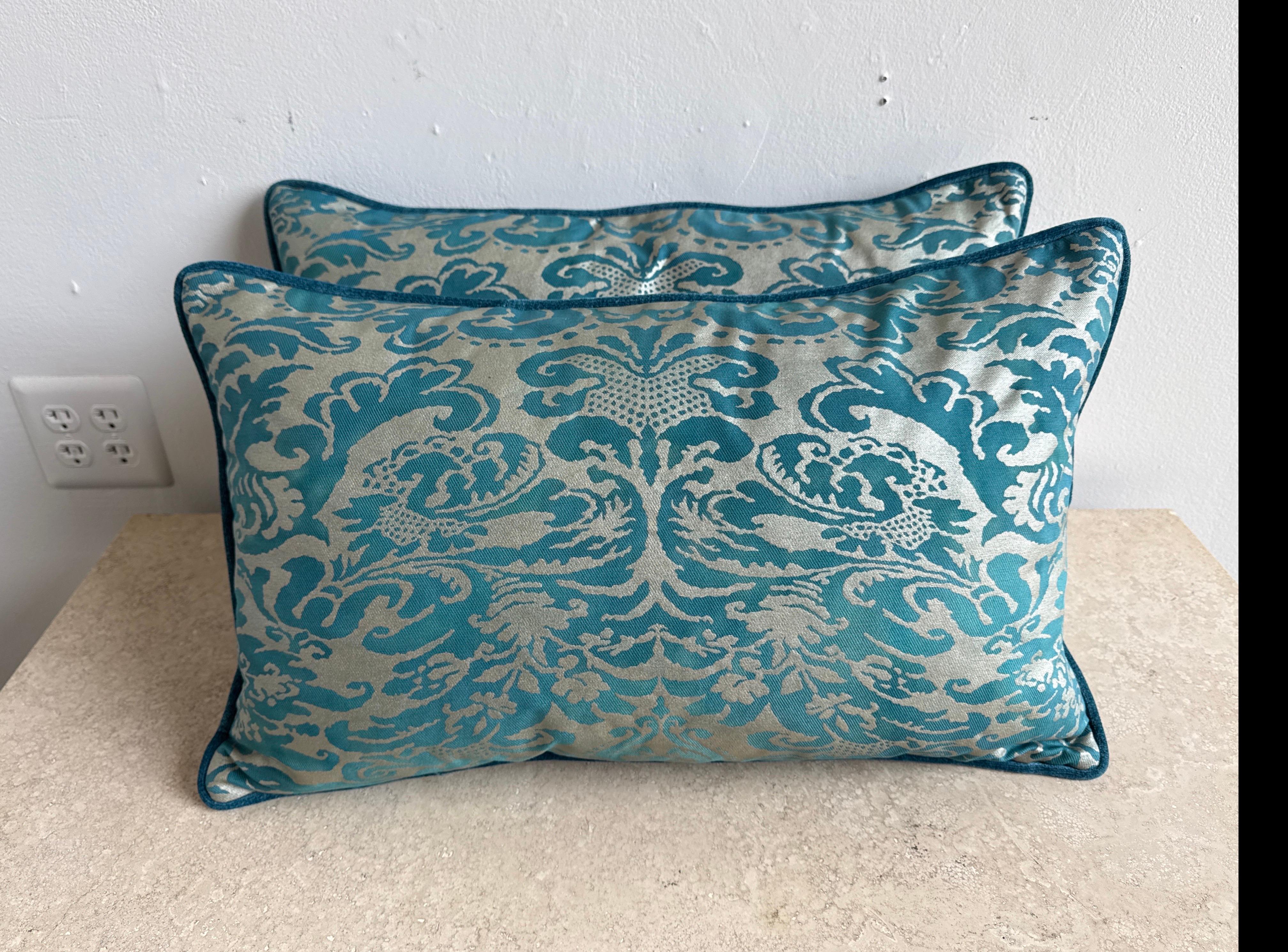 Este elegante par de almohadas presenta frentes textiles Fortuny en un rico estampado de damasco verde azulado y dorado plateado, mostrando el lujoso y consagrado diseño veneciano por el que Fortuny es célebre. El dibujo es intrincado y simétrico,