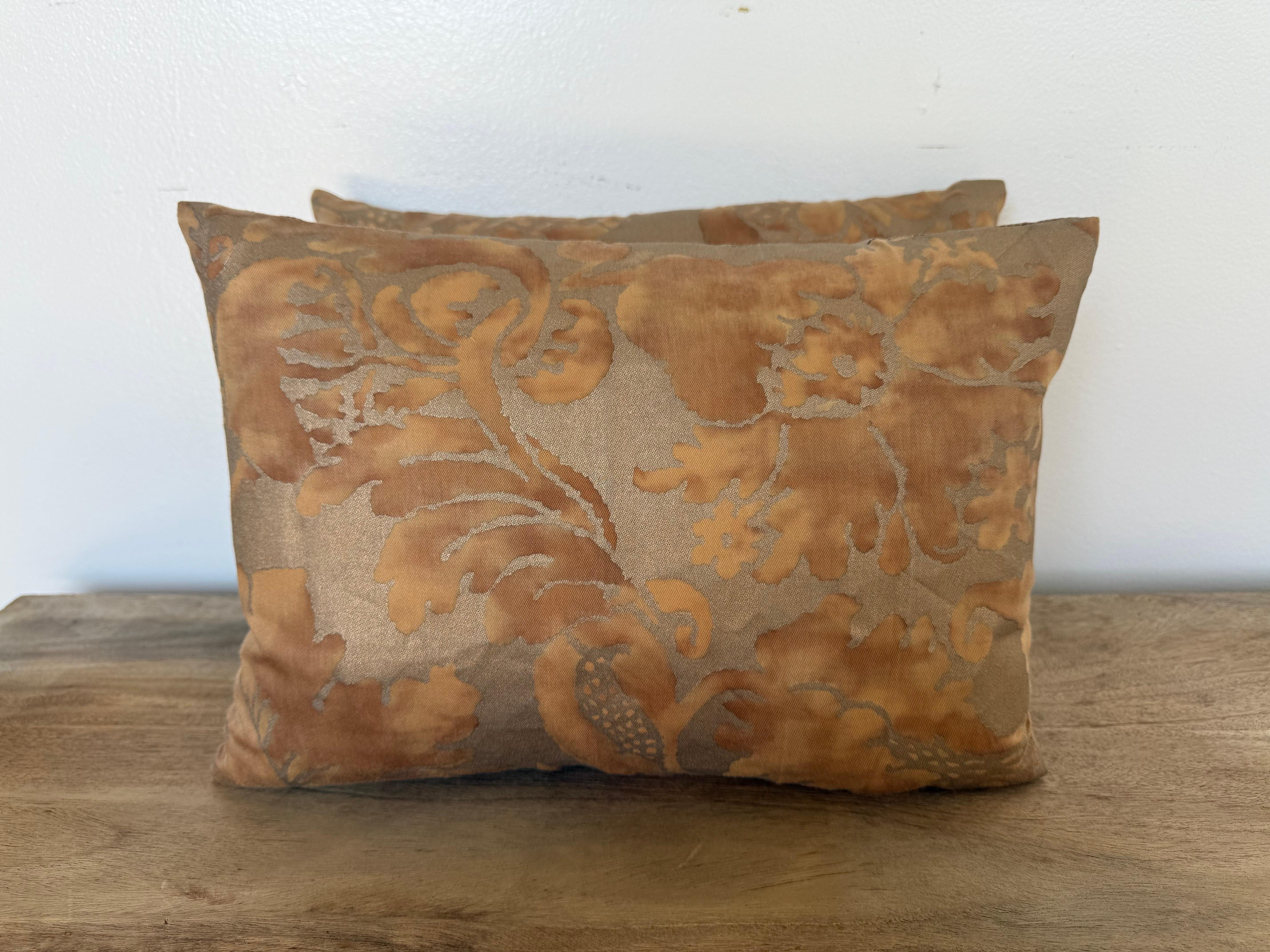 A sophisticated pair of custom pillows designed by Melissa Levinson, showcasing authentic Fortuny textile fronts in warm golden-taupe tones with a subtle faded terracotta floral and foliate pattern. The aged patina of the Fortuny fabric reveals its