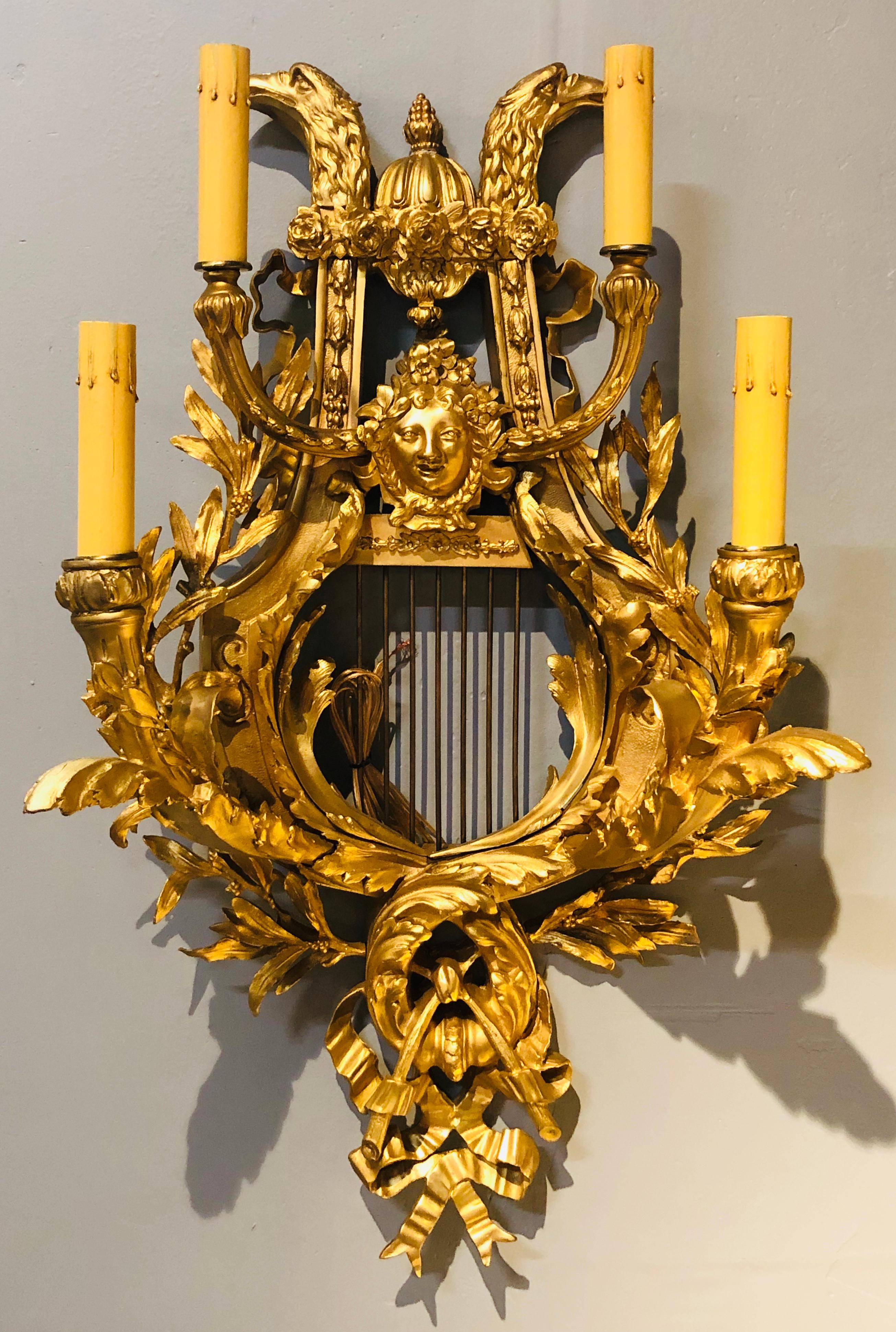 Pair of four-light Louis XVI style bird and face mounted gilt bronze wall sconces. This newly wired and restored pair of gilt bronze wall sconce are sleek and stylish with their harp lyre back supporting a ribbon and tassel bottom with two lower and