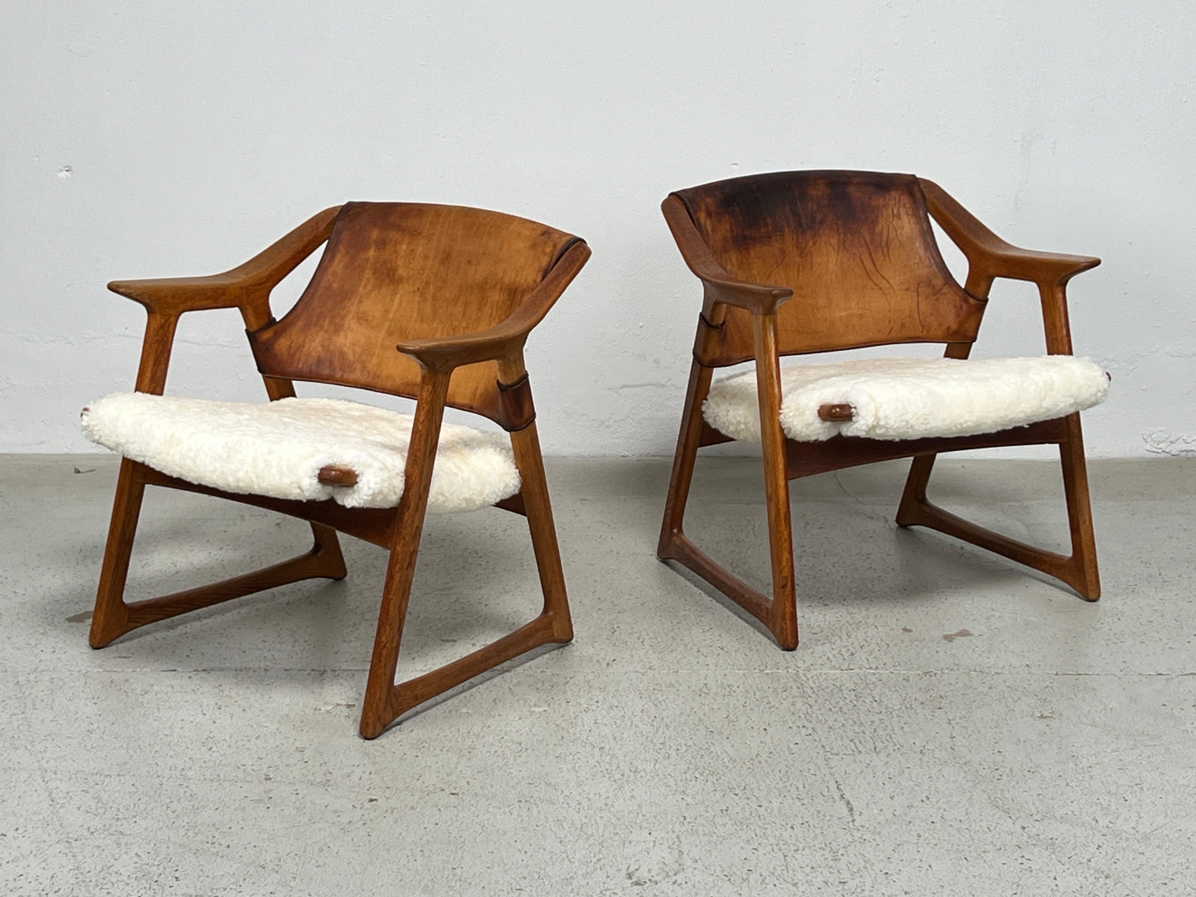 A rare pair of 'Fox' chairs designed by Rolf Hesland in 1958. The oak frames have a rich patina with an older repair to one arm as shown in the photos. The original leather is heavily patinated but structurally sound. The seats have been