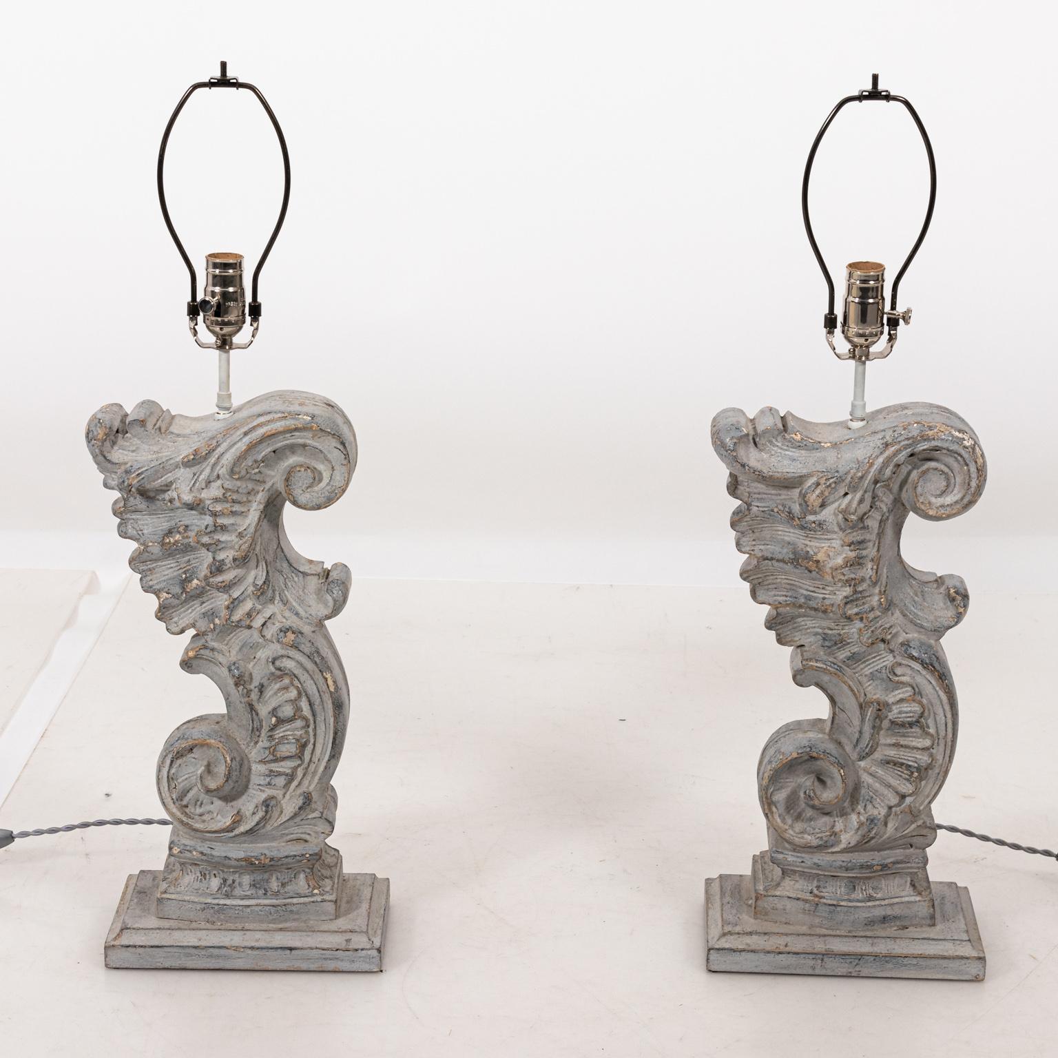 Pair of French Baroque architectural fragments of S-scroll shaped foliage repurposed as table lamps. The pieces also feature a washed gray finish with cream linen shades and glass finials. Please note of wear consistent with age including minor