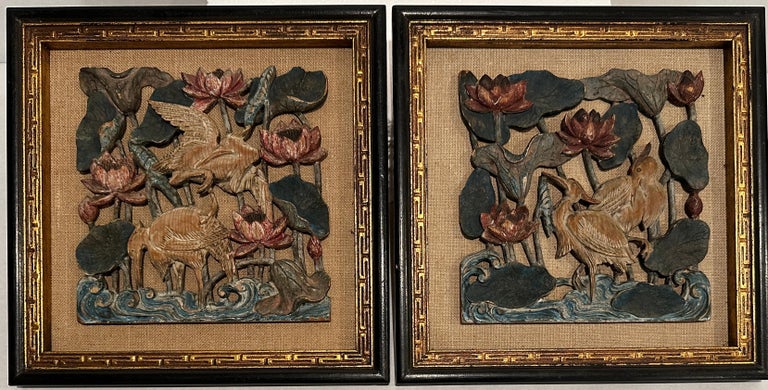 Nicely carved and framed pair of high relief carved and painted panels. Subtle colors with age appropriate worn finish carved depicting cranes (birds) amongst flowers standing in water with curling waves.