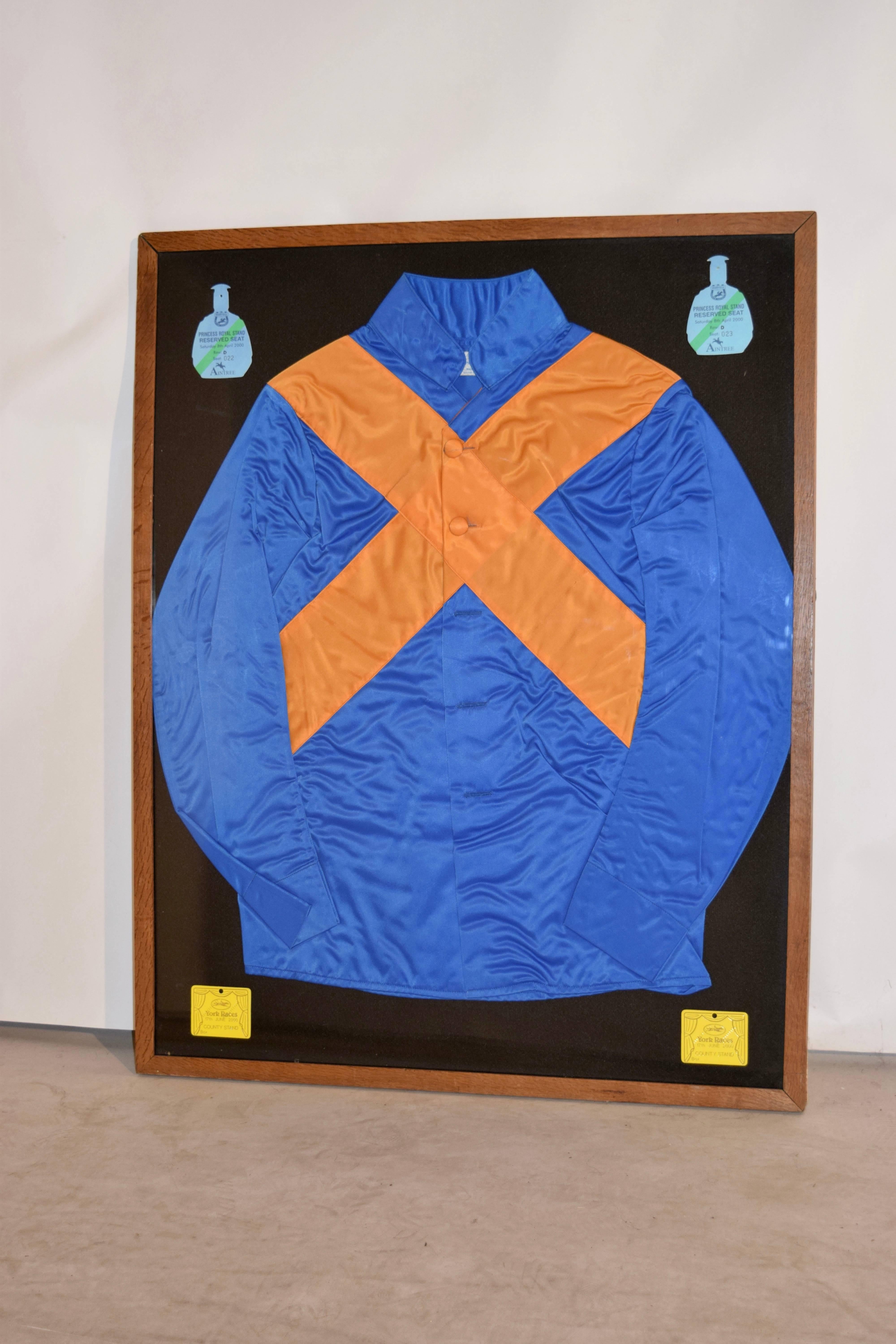 Pair of 20th century jockey silks in frames with race badges in the corners of the frames. Neat decorative accessory.
