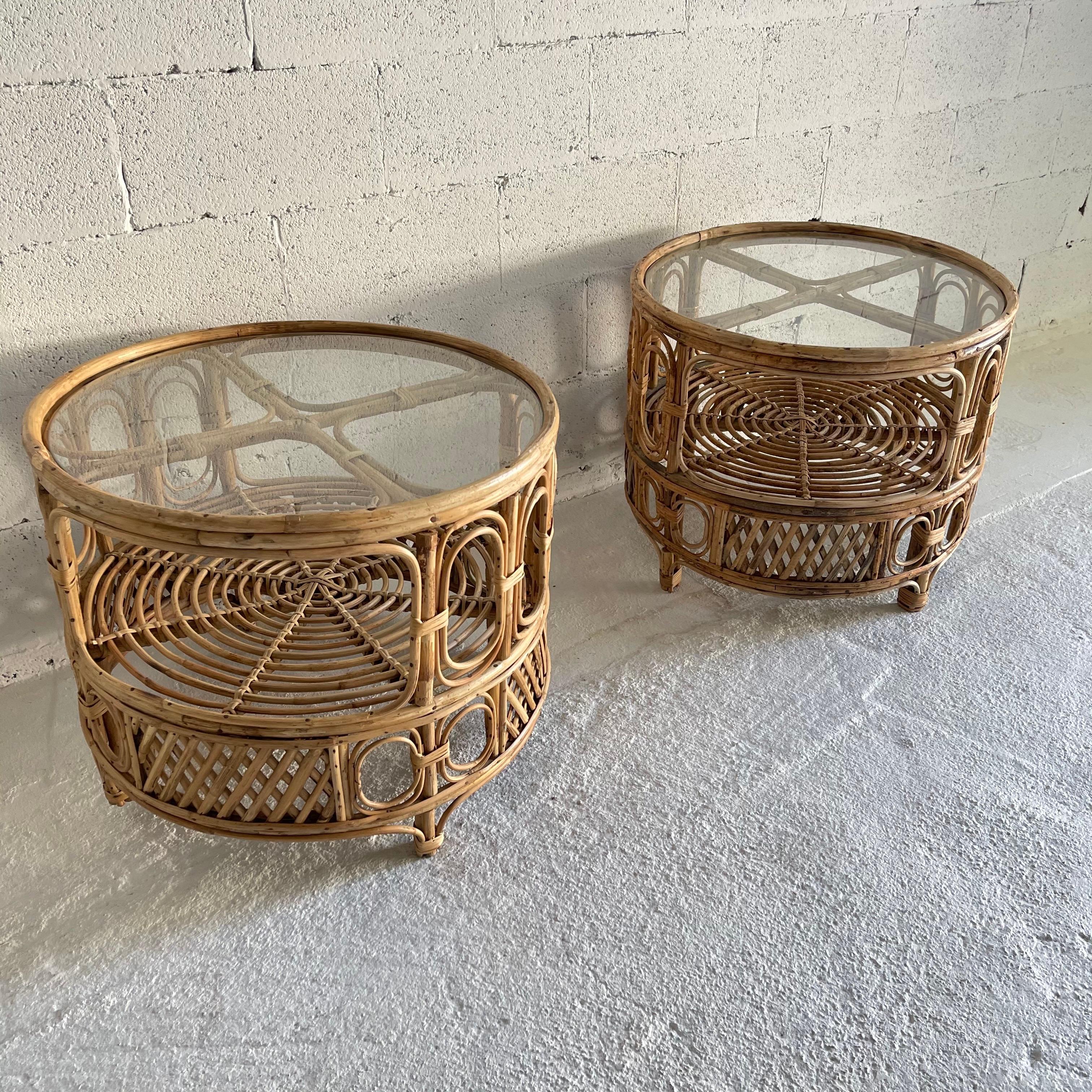 Unique rattan side or end tables in a whimsical design of loops and cross lattice work with an integrated shelf and round glass top, rendered in bent rattan wicker cane reed bamboo, Italy, 1950s.