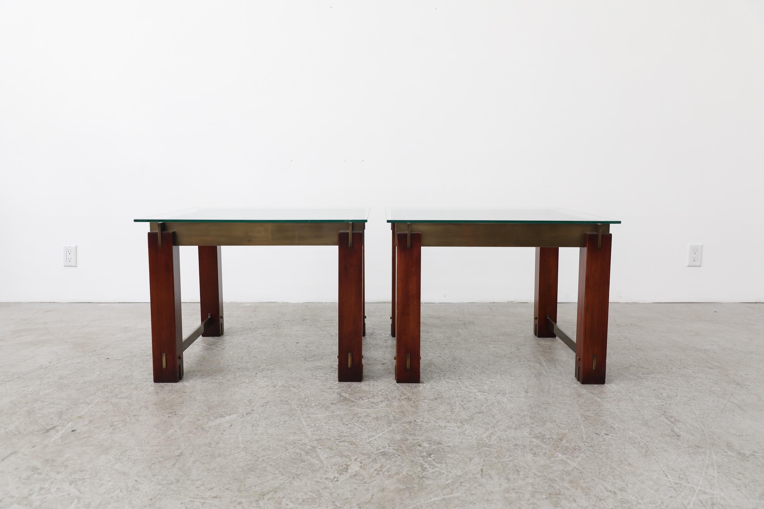 Pair of mid-century side tables inspired by the designs of Frank Lloyd Wright. The matching tables have deep red stain wood legs with handsomely inset brass brass hardware and new glass tops with beveled edges. Glass tops are 27.5