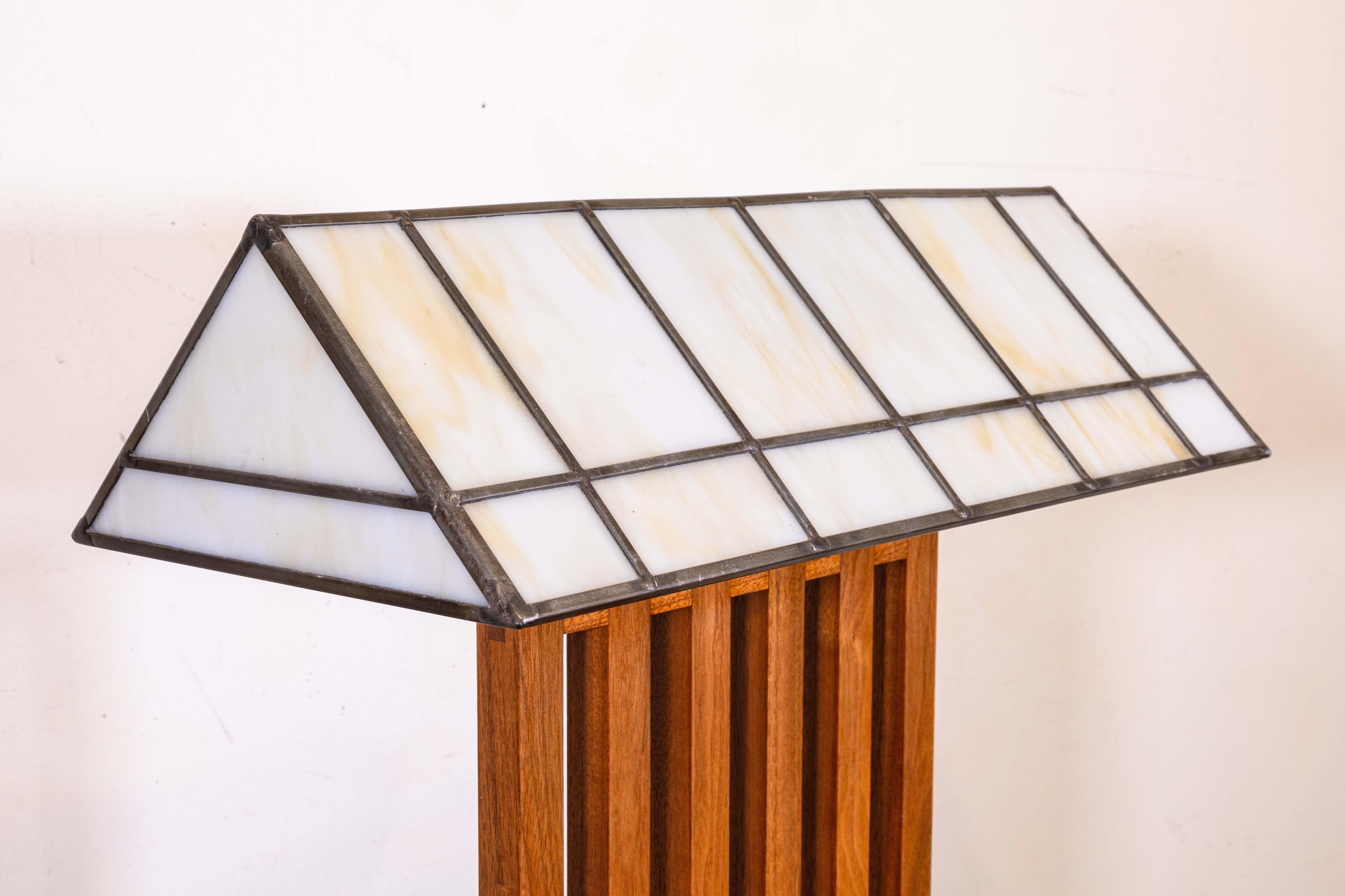 A pair of Frank Lloyd Wright style table lamps. A gorgeous pair of table lamps featuring a full wood frame, and a metal and leaded glass shade. The wood frames feature a series of slatted vertical lines, and a large flat rectangular wooden base. The