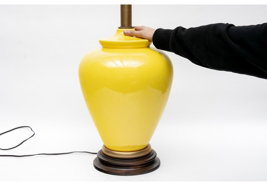 A large bulbous Asian Ginger Jar form in bright yellow glaze, mounted as a table lamp. With a gilt metal base ring on a brown wood base. Brass top mounts and the sockets with Frederick Cooper labels attached. 
H. 24