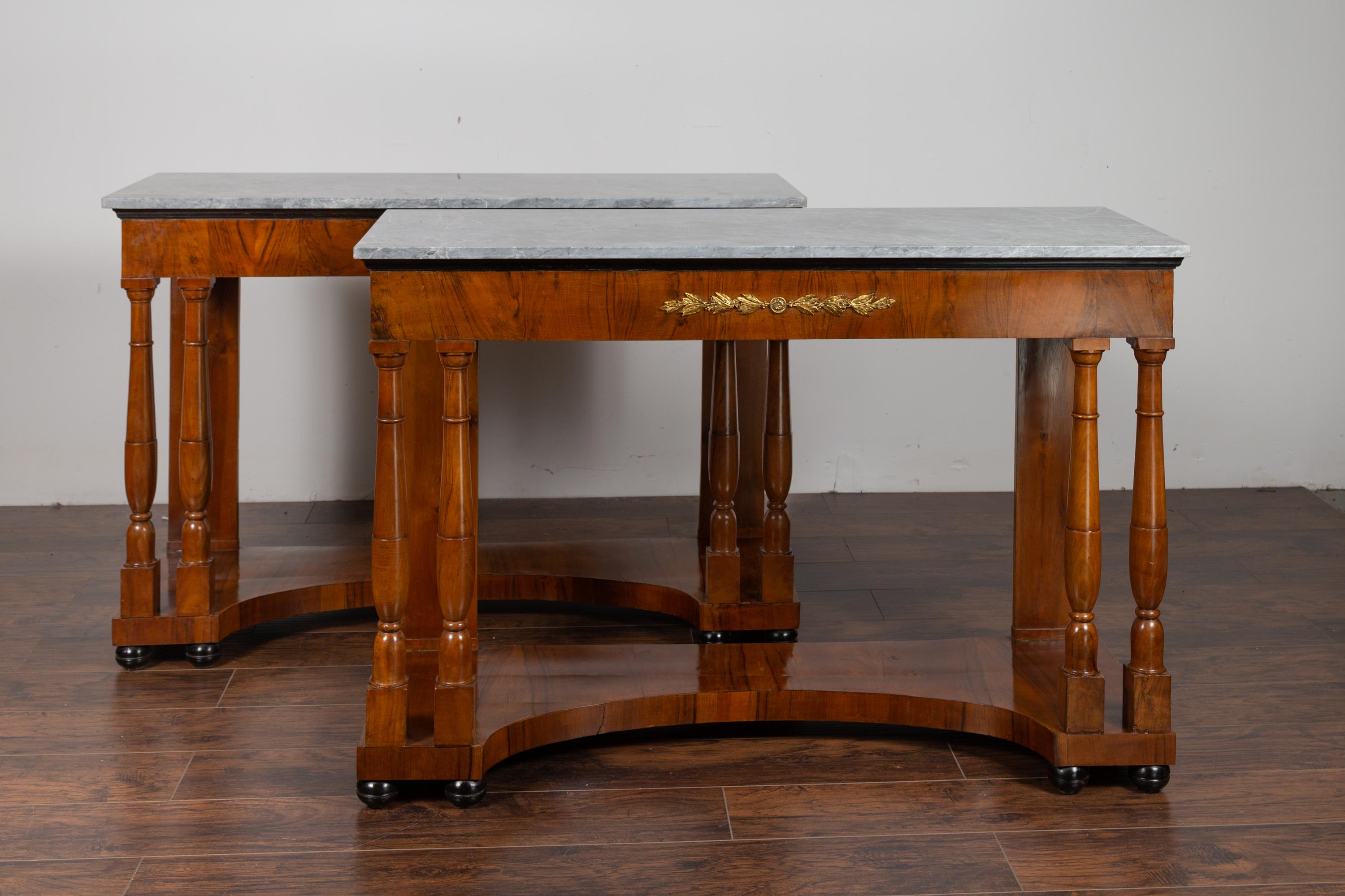 A pair of French Napoleon III period walnut console tables from the mid-19th century, with grey marble tops and bronze motifs. Born in France during the reign of Emperor Napoleon III, each of this pair of console tables features a lovely grey marble