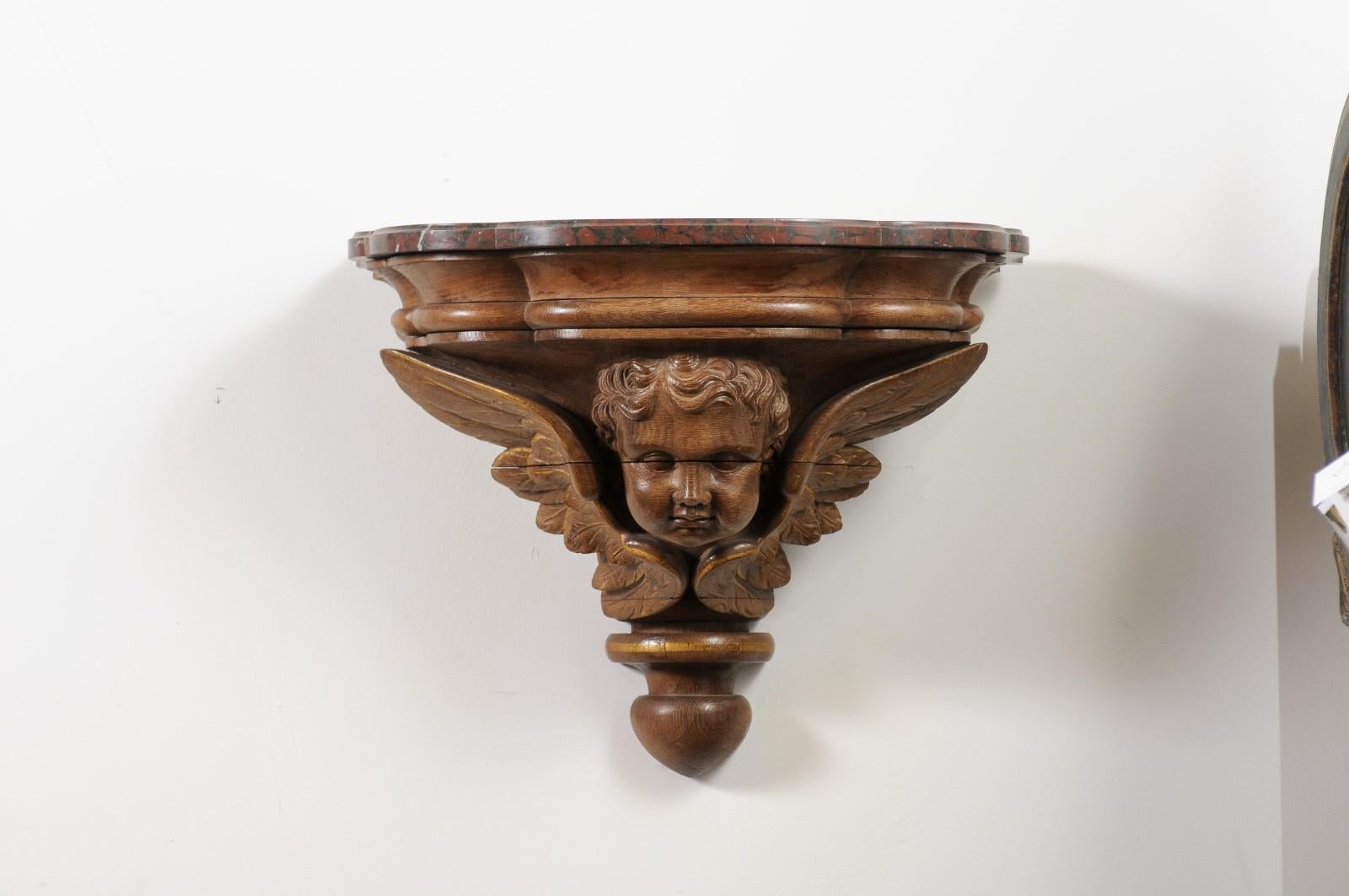 A pair of French carved walnut brackets from the late 19th century, with cherubs and faux marble tops. Created in France during the last quarter of the 19th century, each of this pair of walnut wall consoles features a shaped faux-marble top sitting