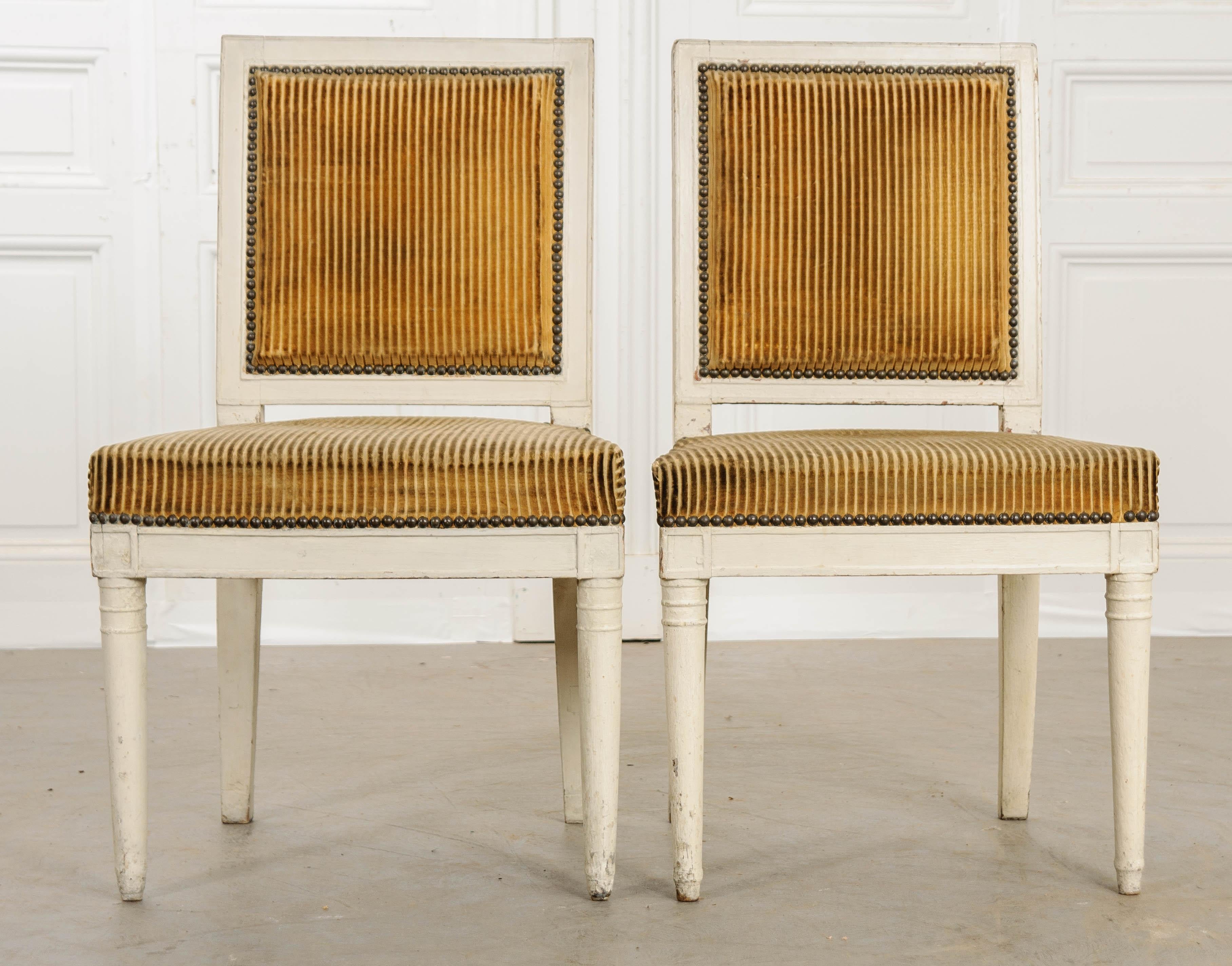 A remarkable pair of period Directoire chairs, upholstered in cut velvet, from 18th century France. Each chair has had their front legs turned in the Directoire style and painted an ivory color that has taken an antiqued patina over the years. The