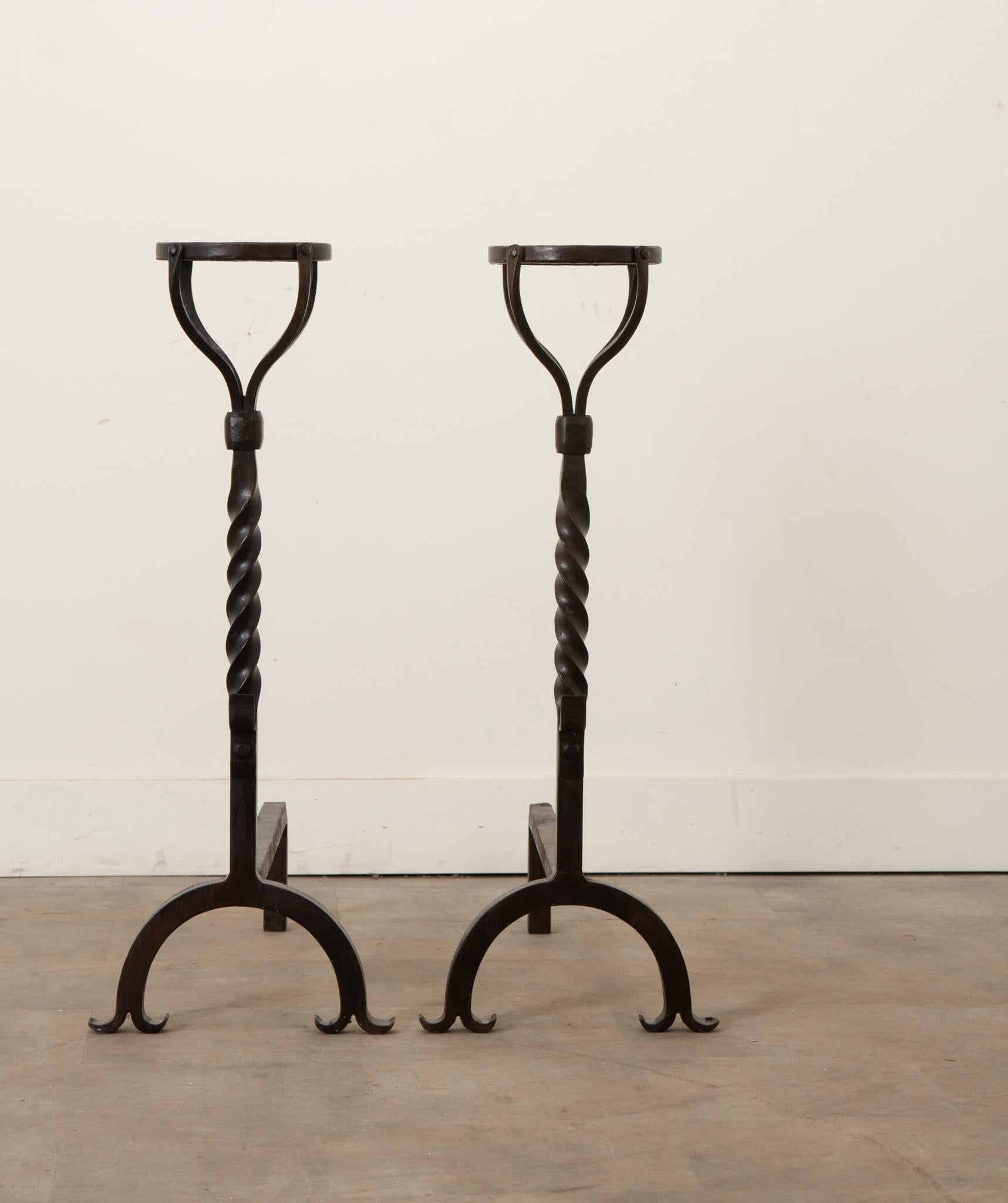 A French pair of hand forged iron andirons. Andirons are works of functional art that dress up your otherwise simple fireplace. Andirons or fire dogs were created to hold logs and for open hearth cooking. The tops of this pair of andirons have